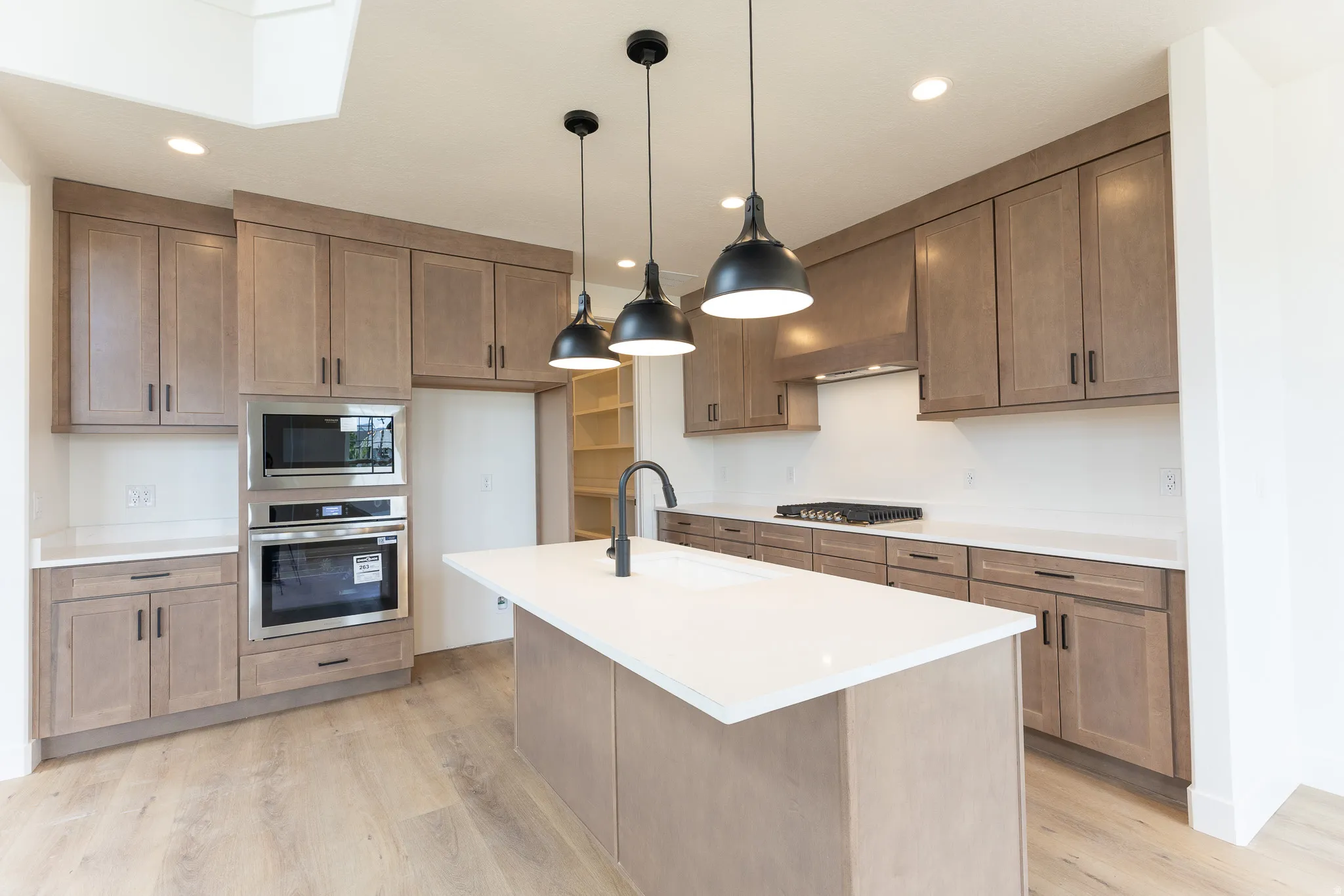 Contemporary kitchen featuring an expansive island with an undermount sink, three pendant lights, wood-finish flooring, and light-toned cabinetry