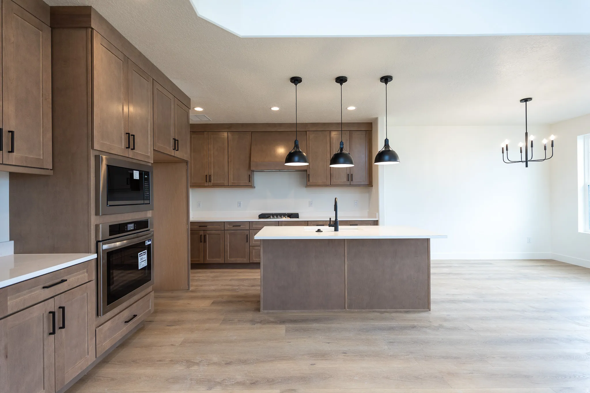 Open-concept kitchen featuring wood-finish cabinetry, built-in stainless steel appliances, a center island with pendant lighting, and light-toned wood-finish flooring