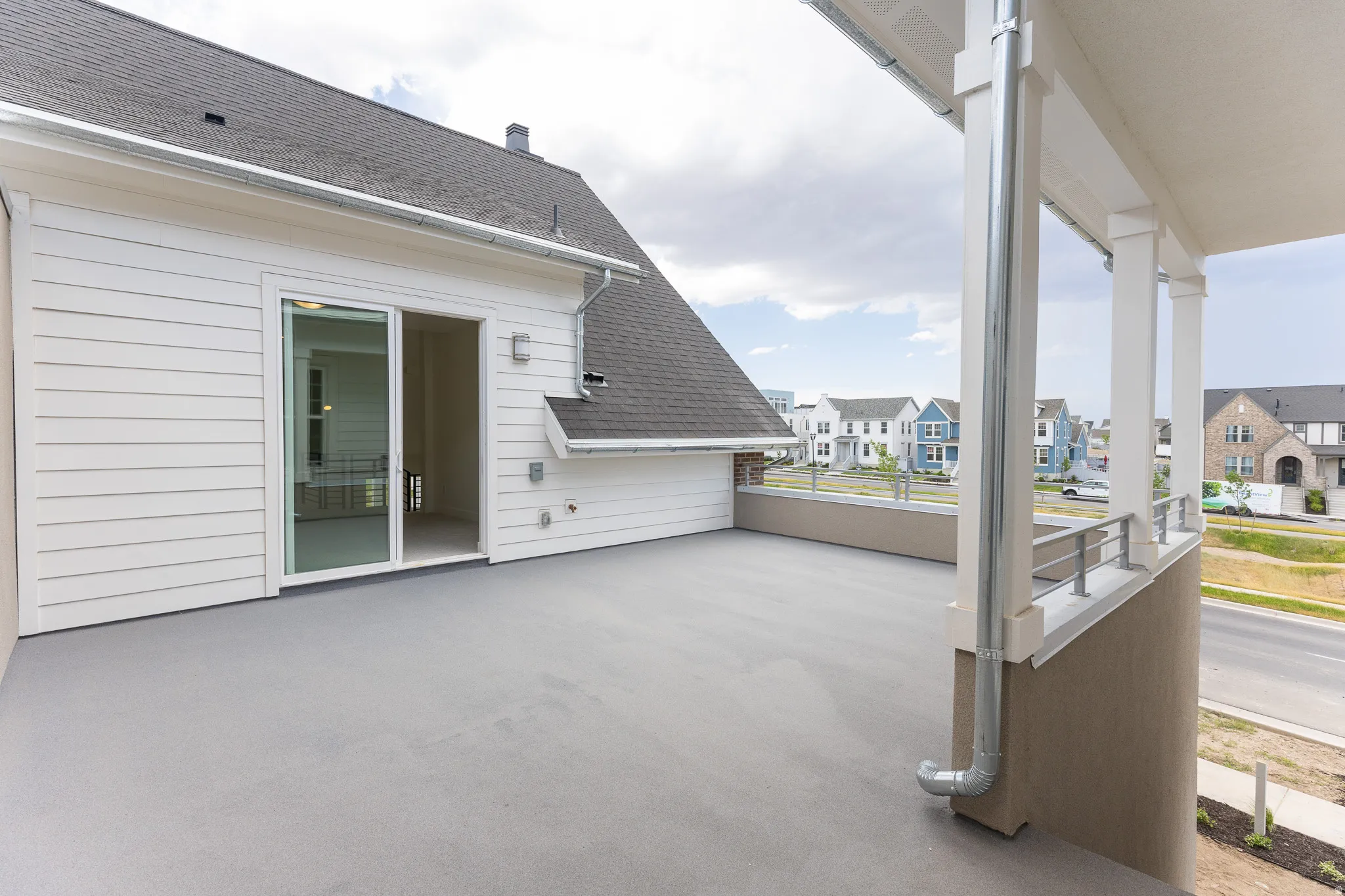 Expansive outdoor balcony featuring a neutral-toned surface, white horizontal siding, a sliding glass door, and column supports