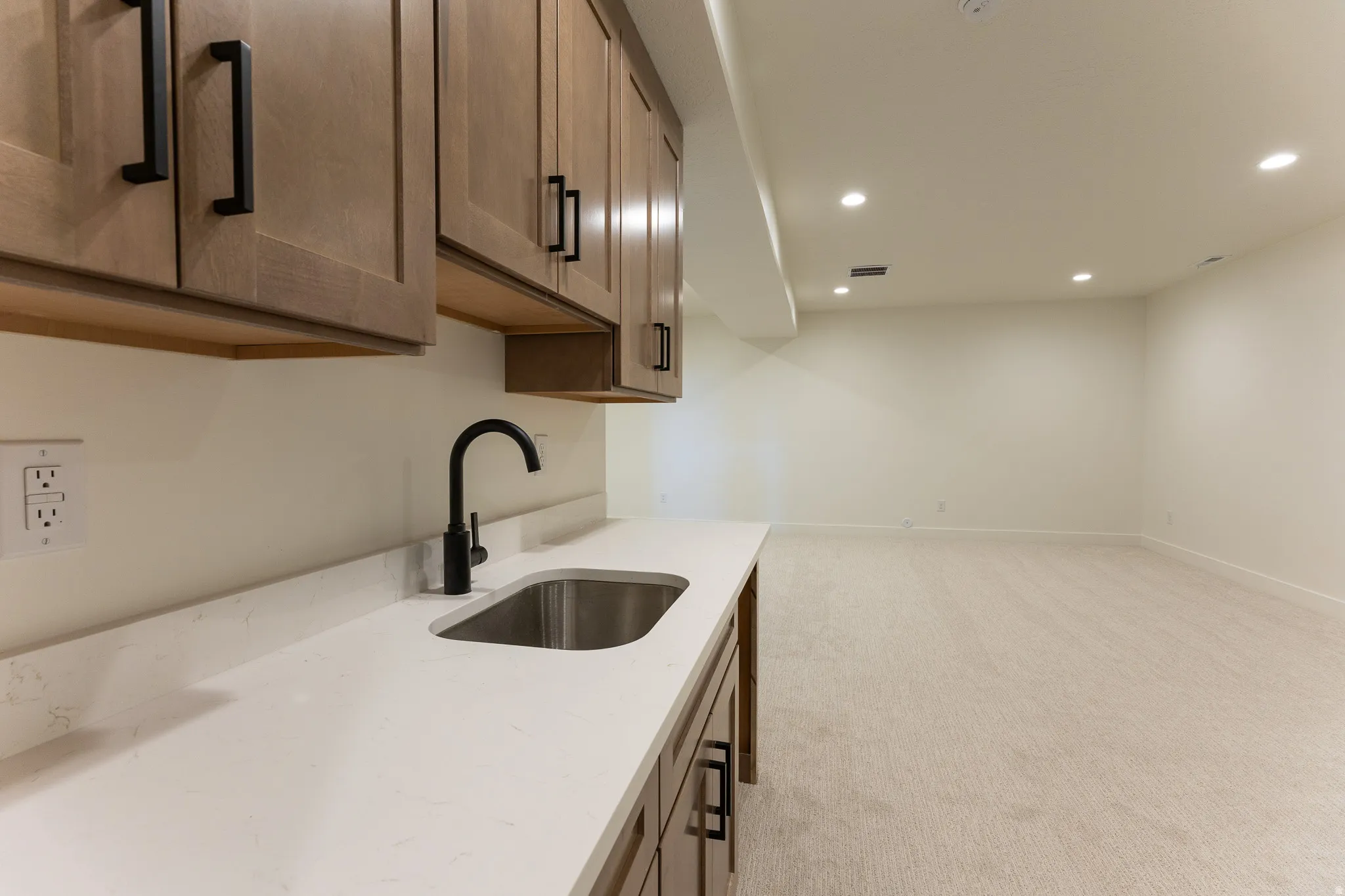 Wet bar featuring light wood-finish cabinetry with matte black hardware, a stainless steel sink, and a black gooseneck faucet