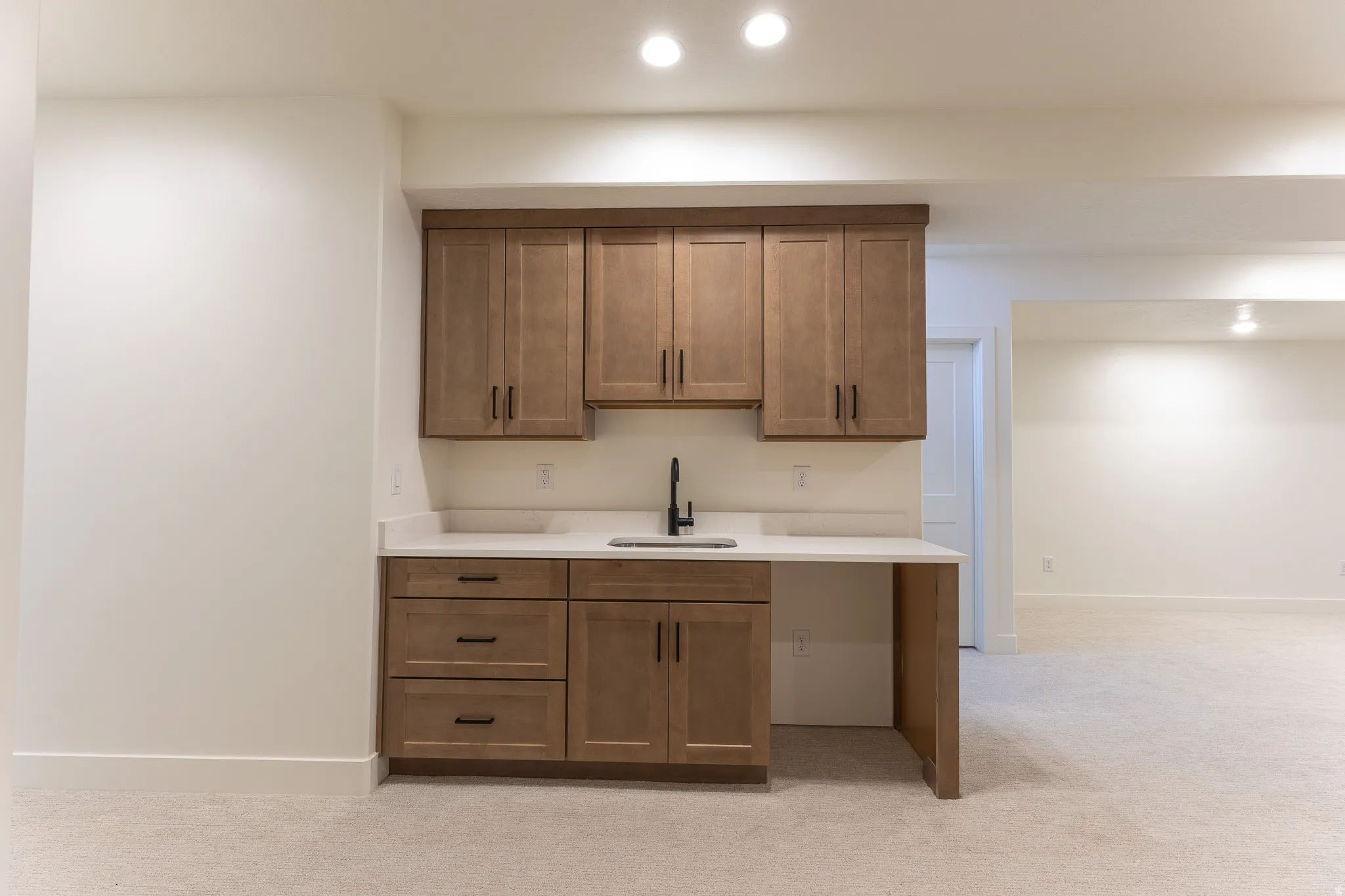 Built-in wet bar featuring wood-finish cabinetry, a white countertop, and a matte black faucet