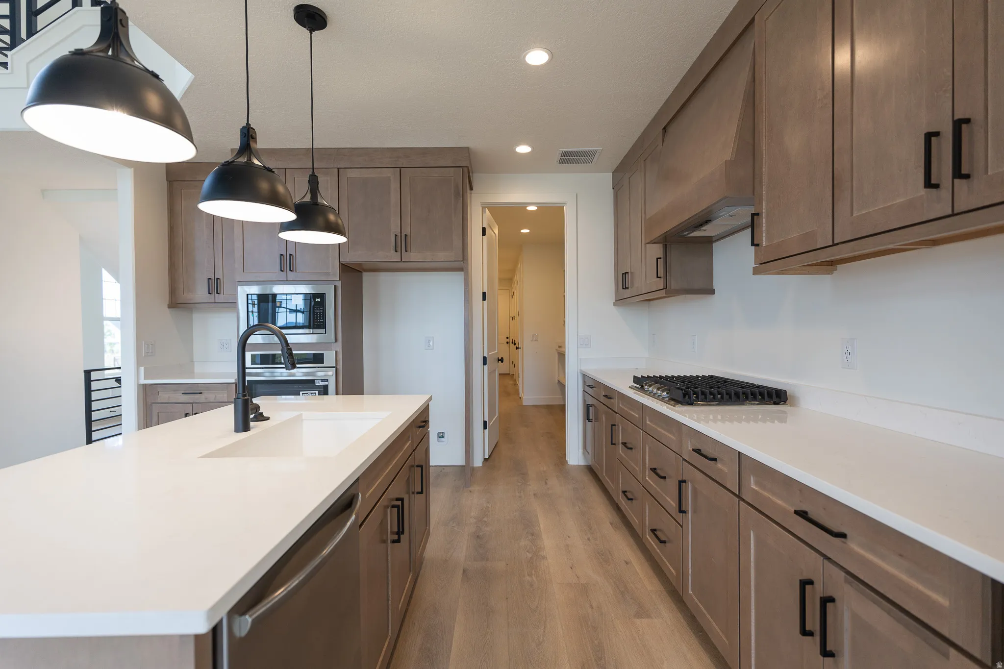 Kitchen featuring a central island with an integrated sink, light-toned wood-finish cabinetry, stainless steel appliances, and white countertops