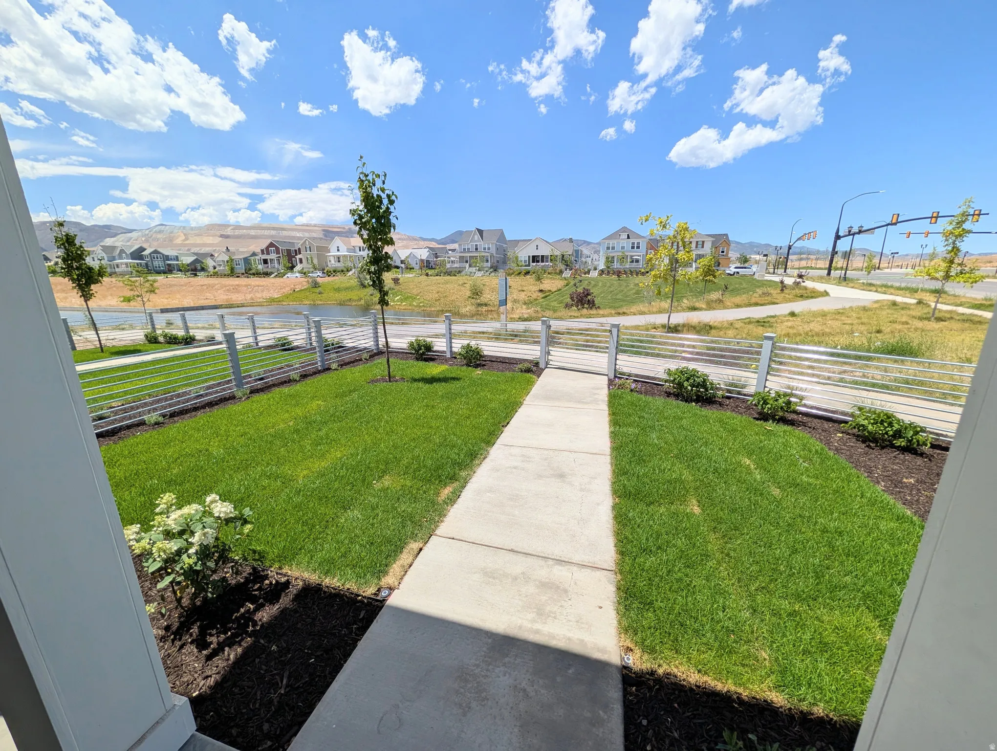 Manicured front yard with a concrete pathway, young trees, and a modern wire fence