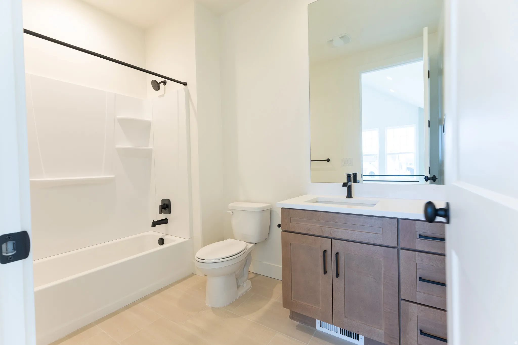 Bathroom featuring a white tub/shower combination with matte black fixtures, a contemporary vanity with wood-finish cabinetry, a white countertop with an integrated sink, a rectangular wall-mounted mirror, and tile flooring