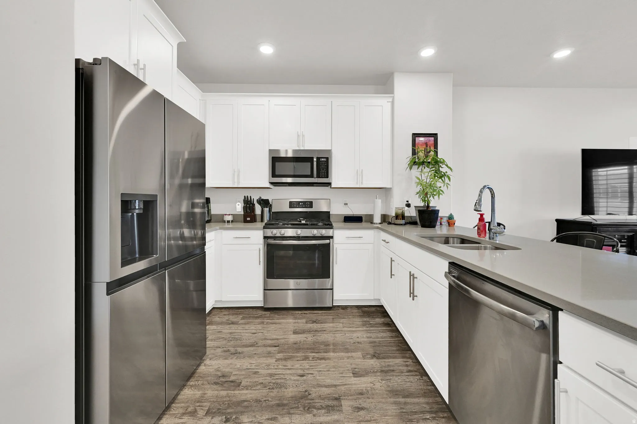 Modern kitchen featuring wood-finish flooring, white cabinetry with contemporary hardware, stainless steel appliances, light-toned countertops, and recessed lighting