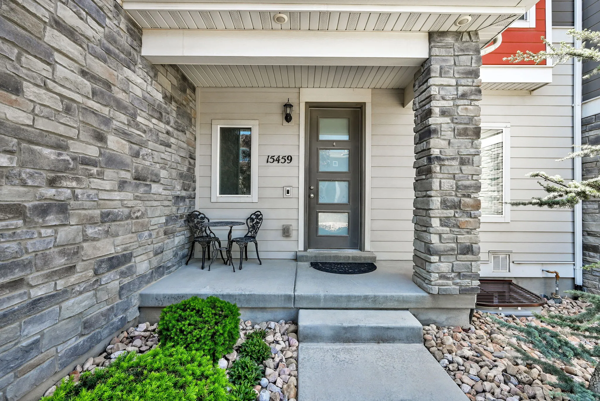 Stone accent exterior featuring a covered entry, contemporary dark-paneled door with frosted glass inserts, and a concrete porch
