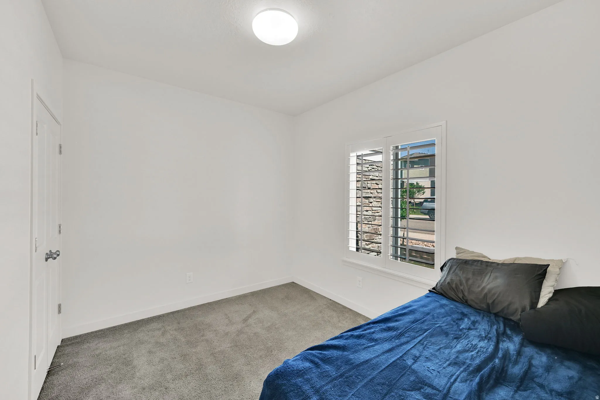 White-painted interior room featuring a window with plantation shutters, gray carpeting, a flat panel door, and a flush-mount ceiling light fixture