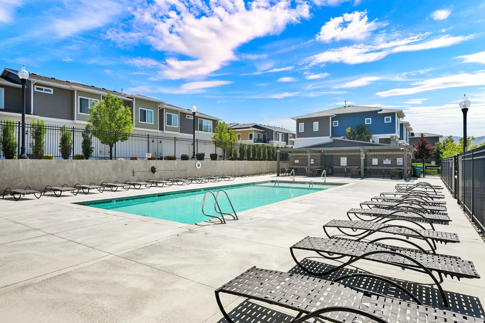 Community swimming pool with concrete decking, surrounding lounge seating, and a covered patio area
