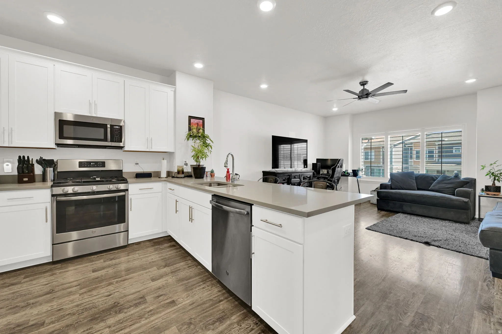 Open-concept kitchen featuring white shaker cabinetry, stainless steel appliances, and a central island with a sink