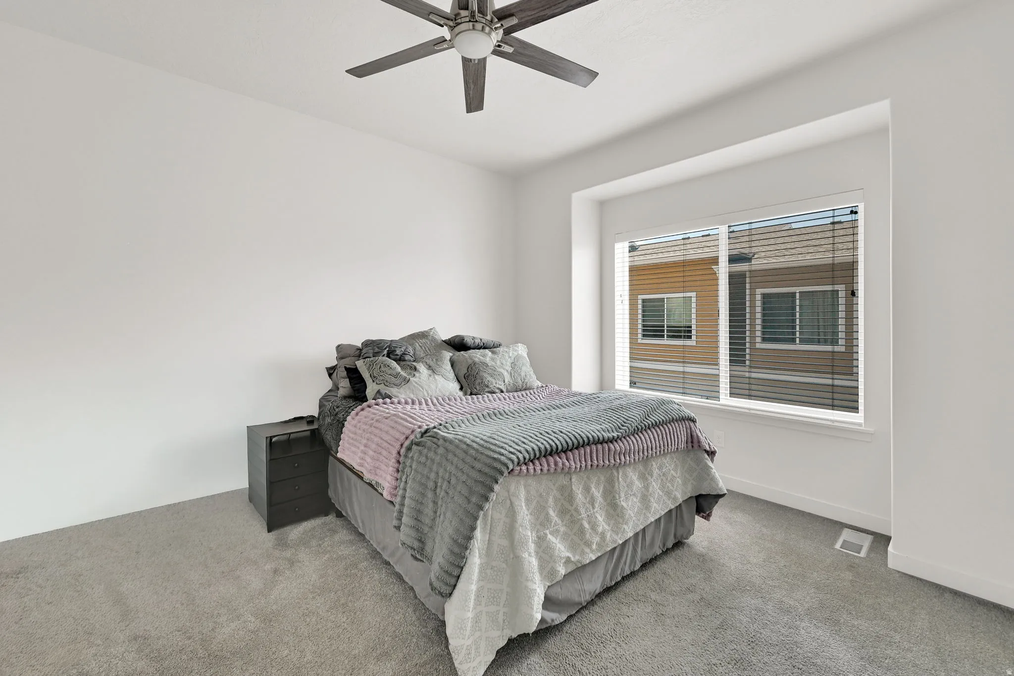 Spacious room featuring neutral carpeting, a modern ceiling fan, and a large window with horizontal blinds
