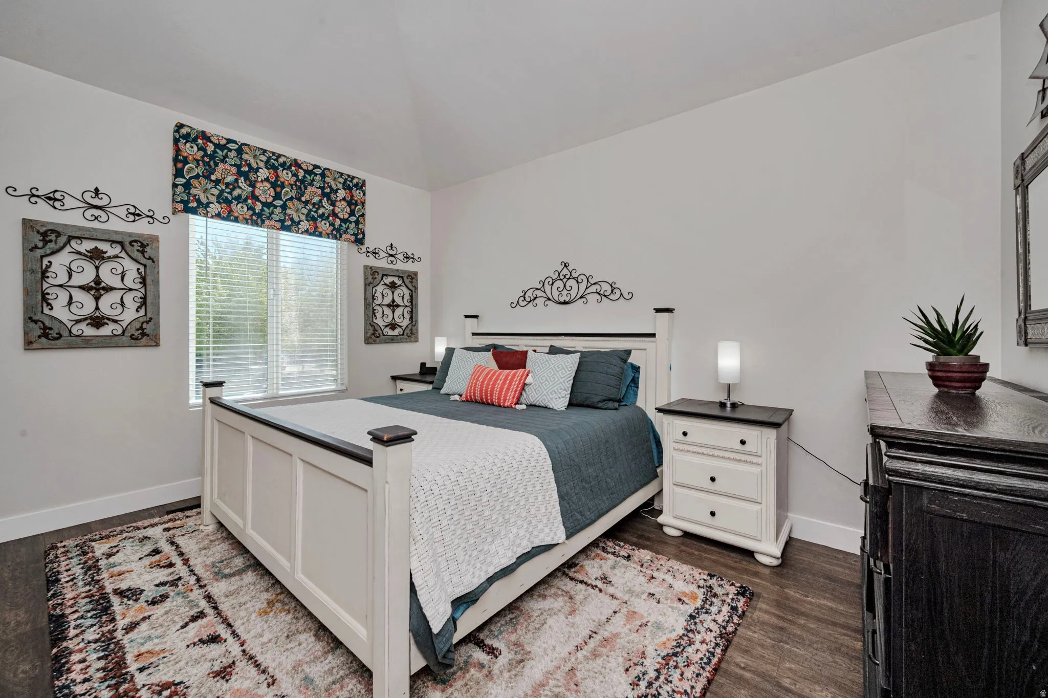 Bright bedroom featuring wood-finish flooring, white baseboards, and a large window with horizontal blinds