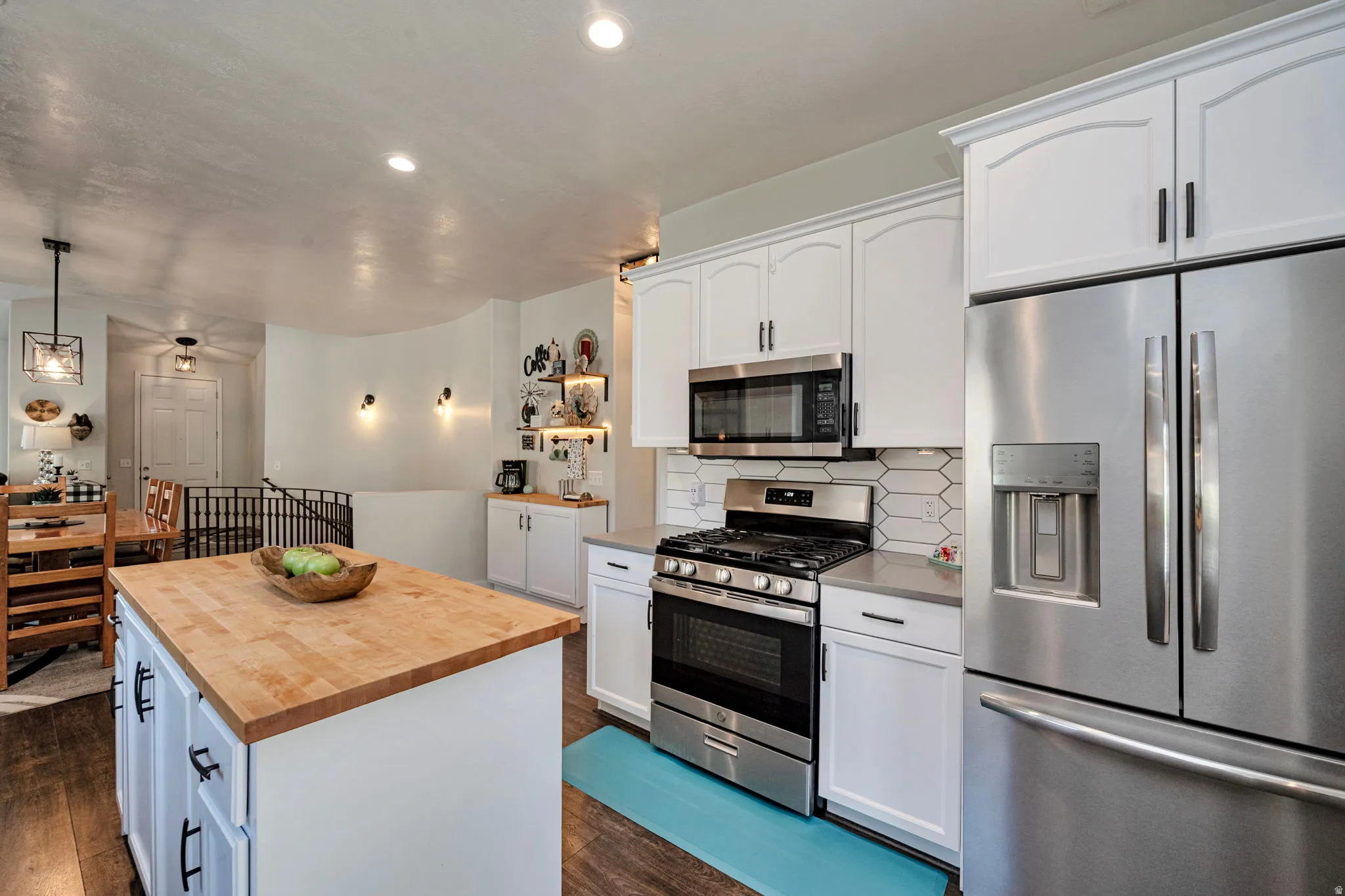 Kitchen featuring a wood-finish island, white cabinetry, stainless steel appliances, and a geometric tile backsplash