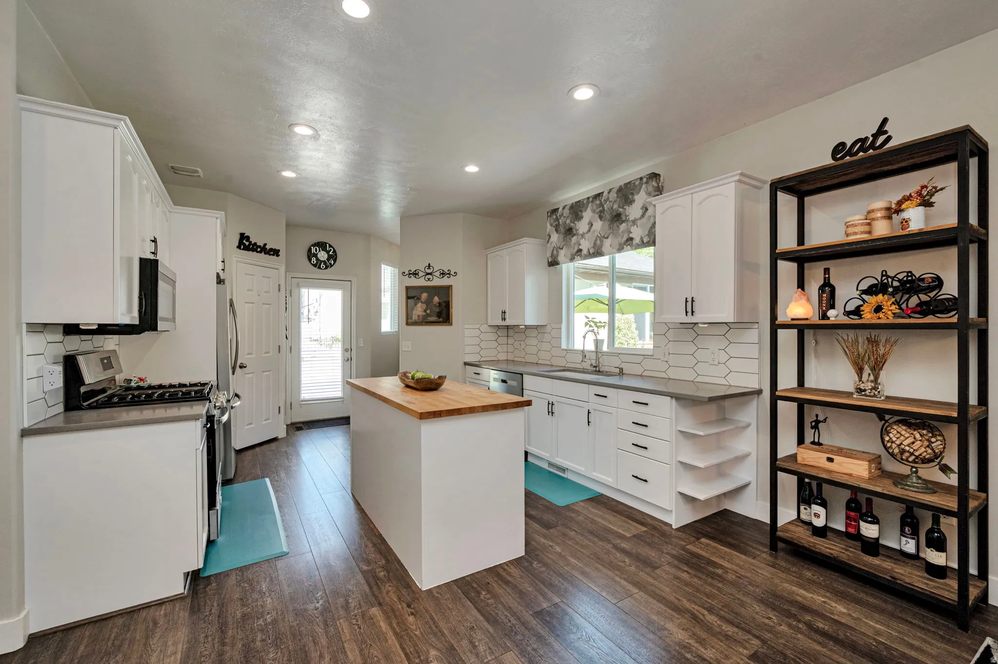 Kitchen featuring wood-finish flooring, white cabinetry, a central island with wood countertop, light-colored countertops, and a subway tile backsplash