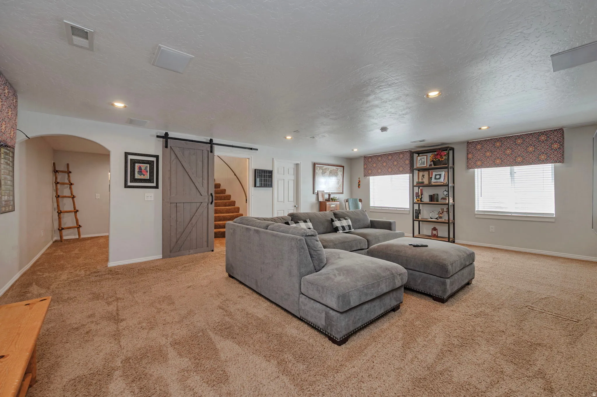 Spacious carpeted room featuring a barn door entry, multiple windows with blinds, and recessed lighting