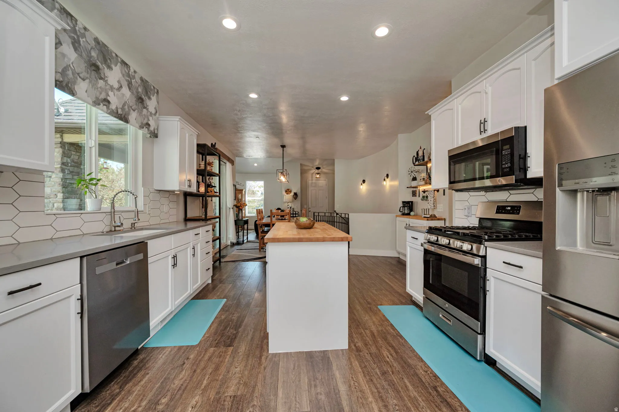 Contemporary kitchen featuring white cabinetry, stainless steel appliances, wood-finish flooring, a central island with a butcher block countertop, and a white hexagonal tile backsplash