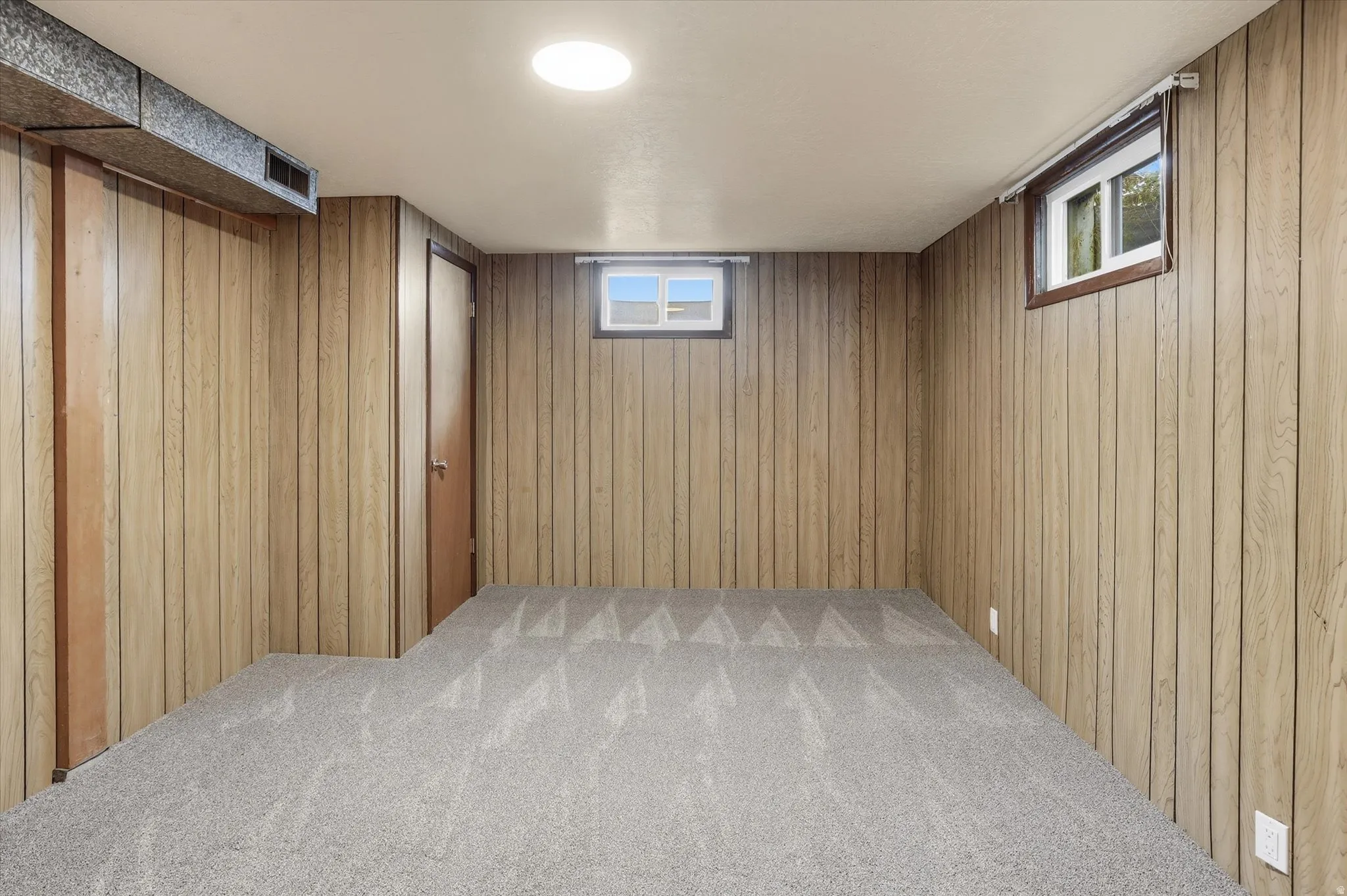 Room featuring light wood paneling, gray patterned carpeting, a white ceiling, and two small windows