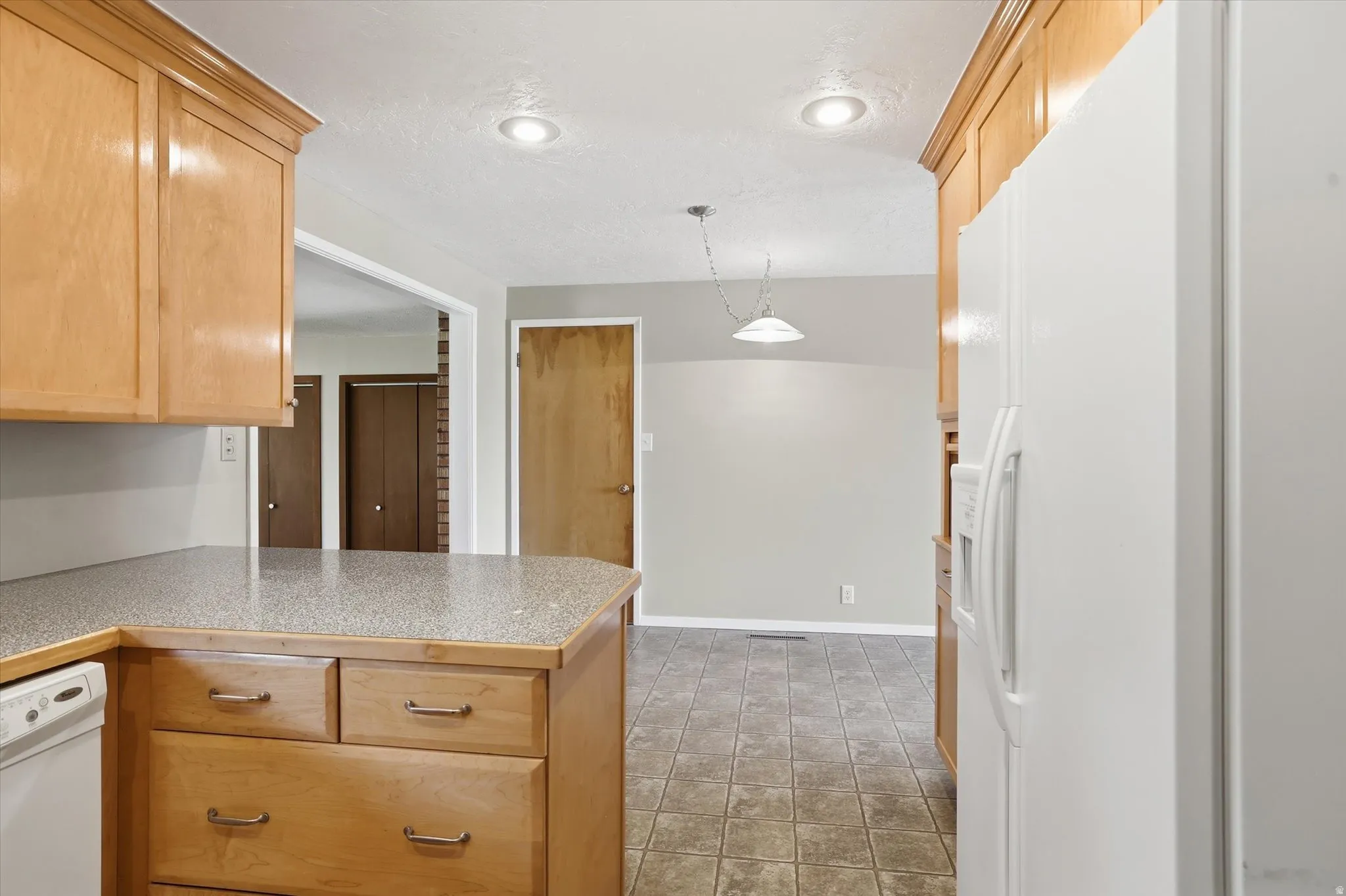 Kitchen featuring wood-finish cabinetry, speckled countertops, recessed lighting, and tile flooring