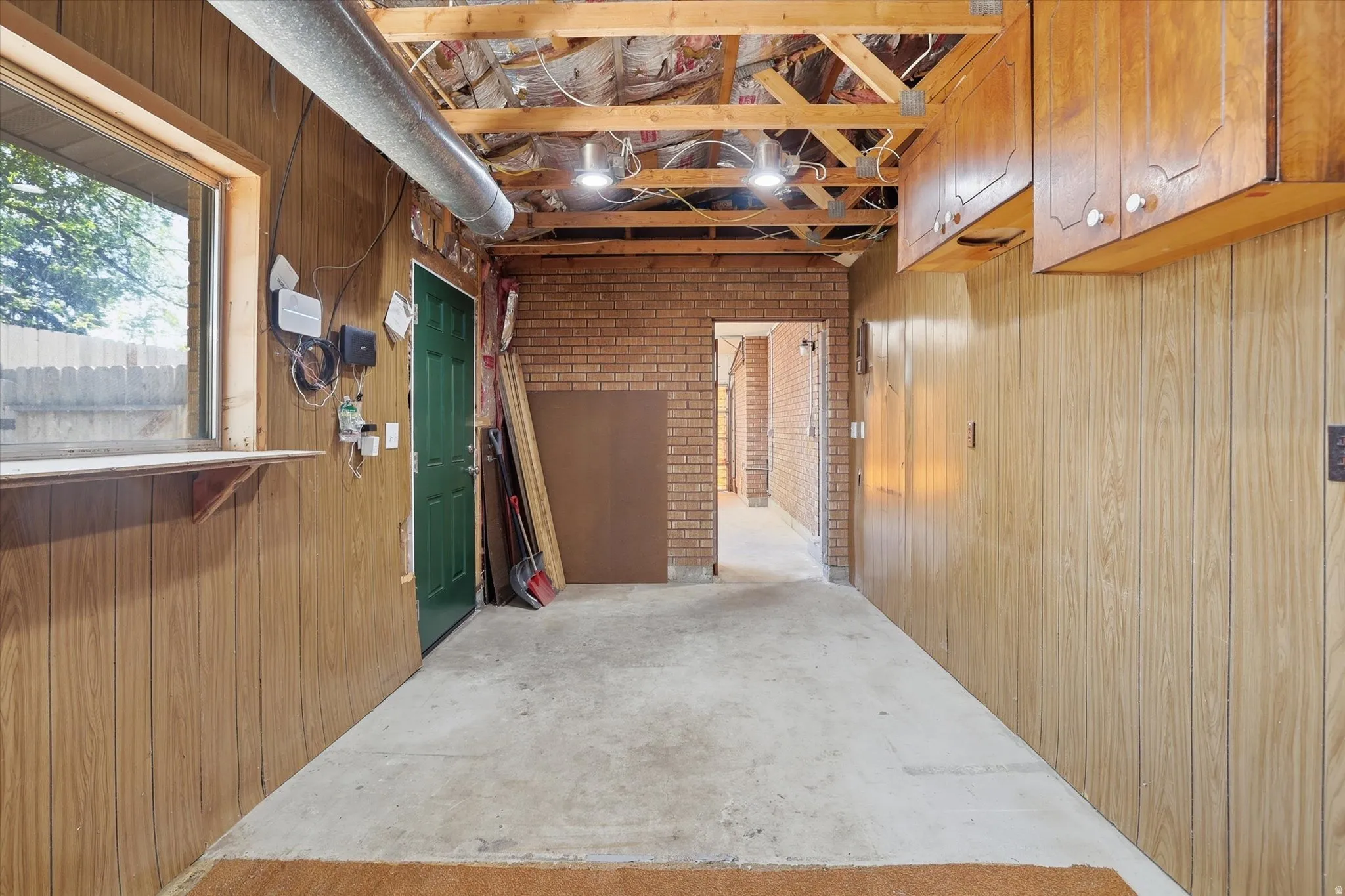 Utility space featuring exposed ceiling joists, wood-finish wall paneling, and an exposed brick accent wall