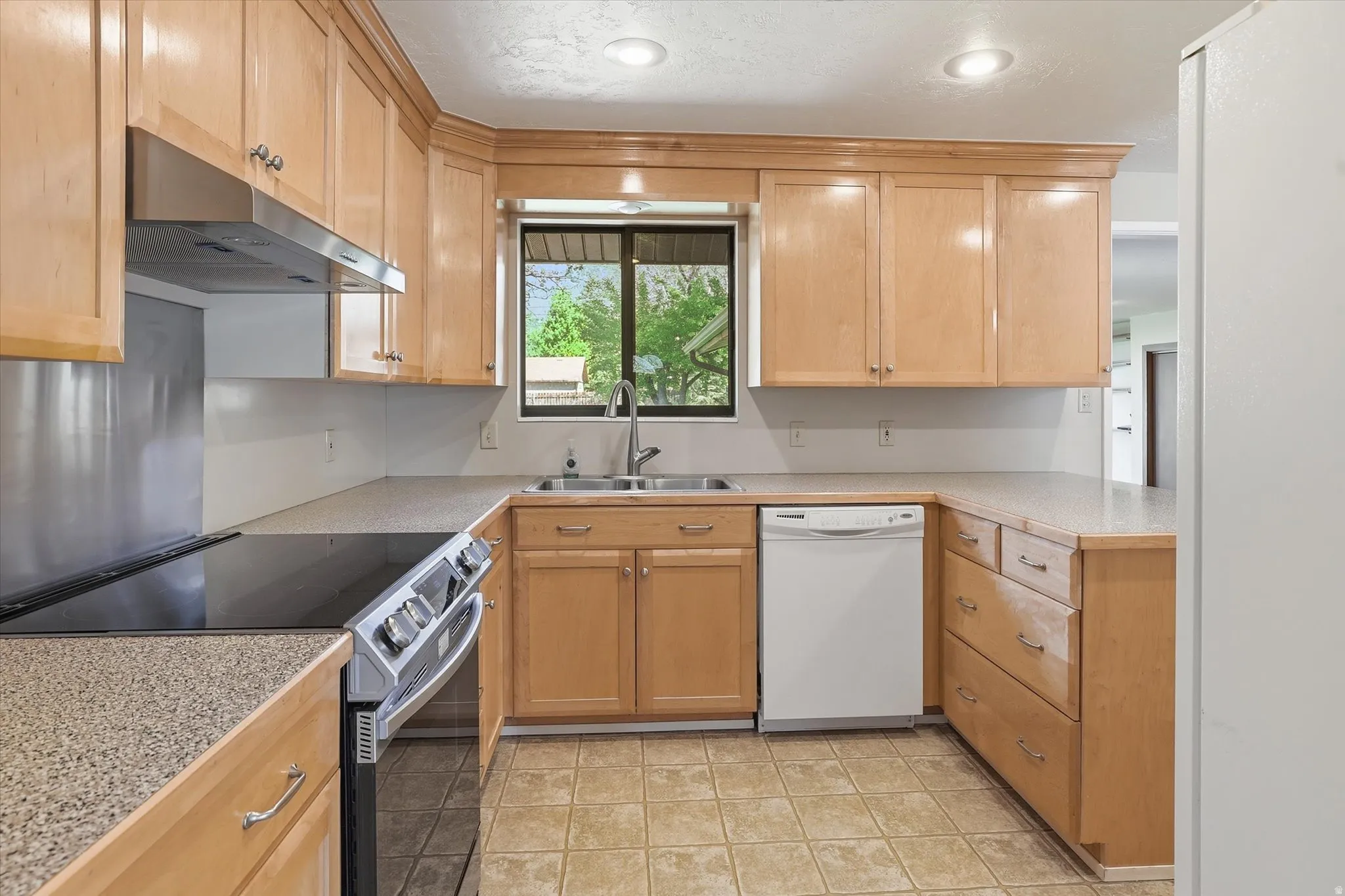 U-shaped kitchen featuring wood cabinetry, speckled countertops, a stainless steel range hood, and a window above the sink