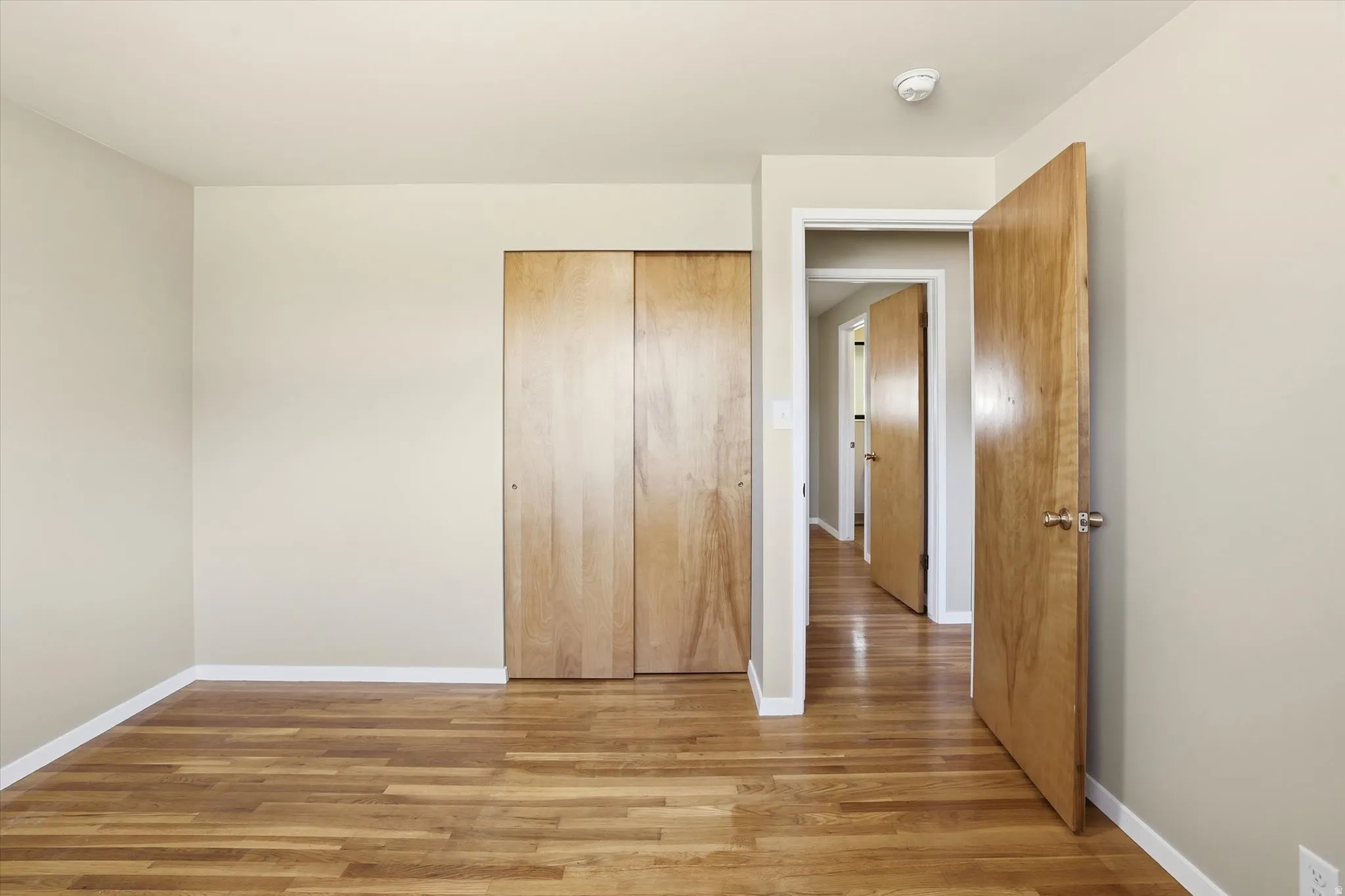 Room featuring wood-finish flooring, light-toned walls, white baseboards, and a built-in closet with wood-panel sliding doors