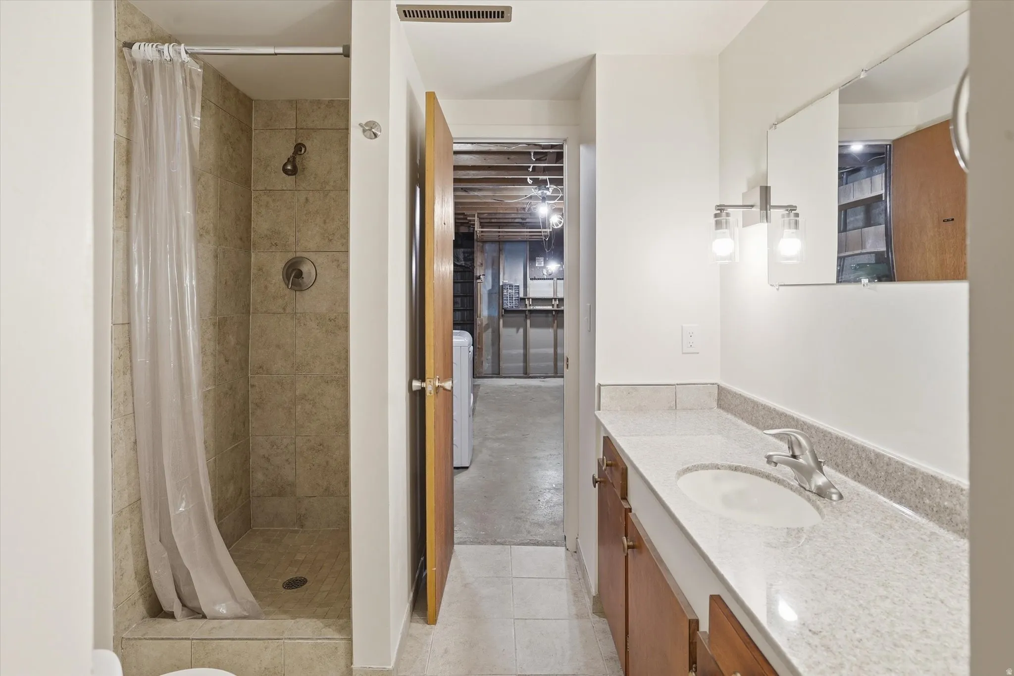 Bathroom featuring a tiled shower with brushed nickel fixtures, a vanity with a light-colored countertop, and a rectangular mirror