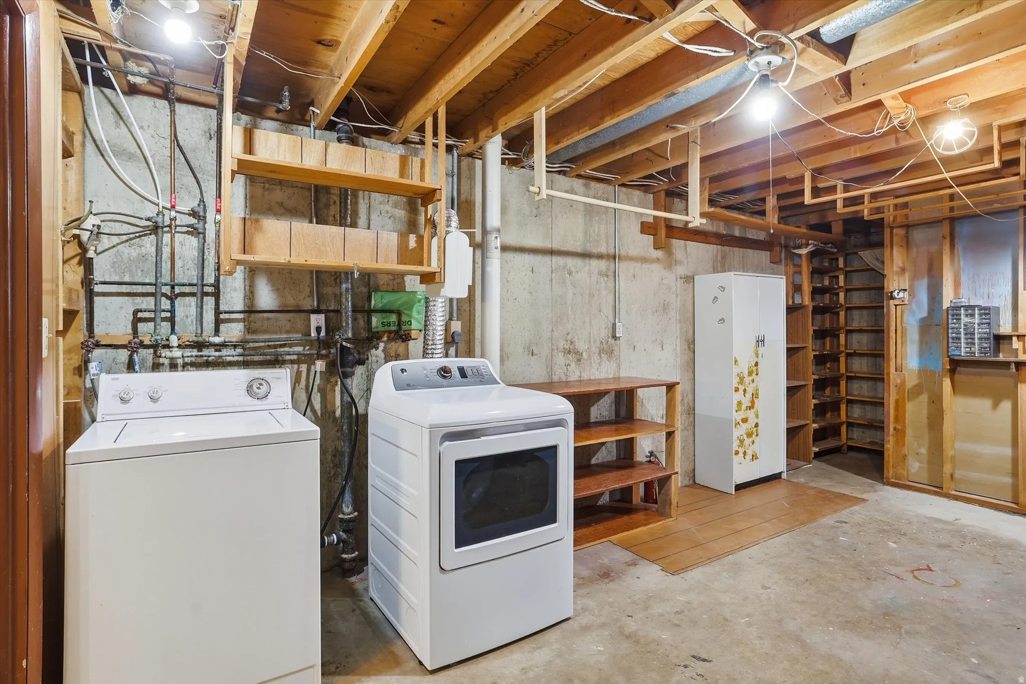 Unfinished basement with laundry area featuring exposed ceiling joists and concrete walls