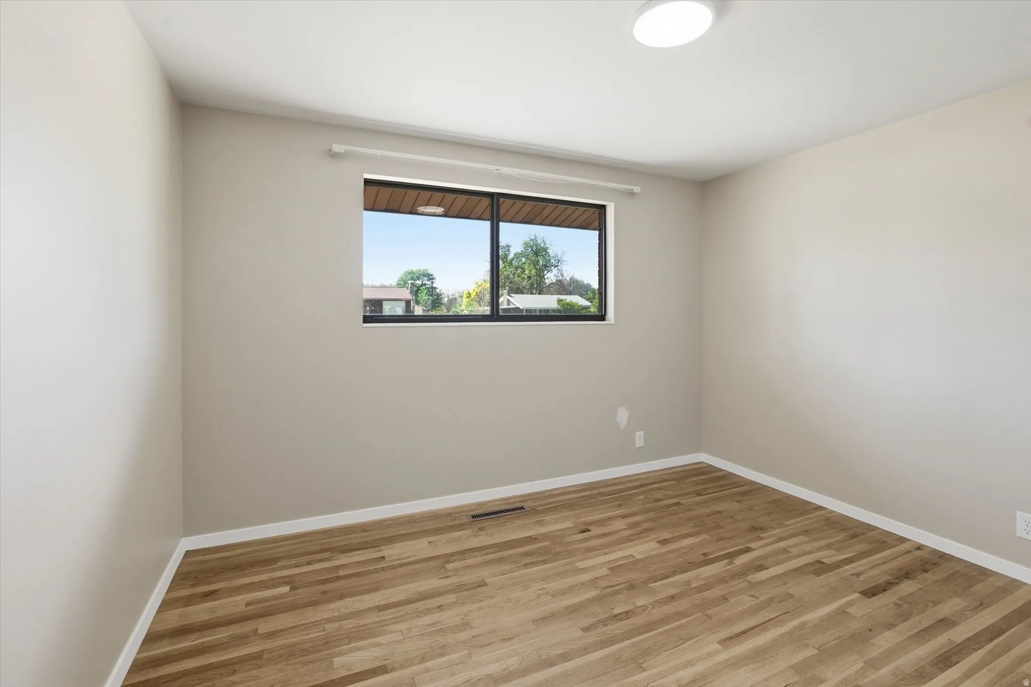 Neutral-toned room featuring wood-finish flooring, white baseboards, and a large black-framed window