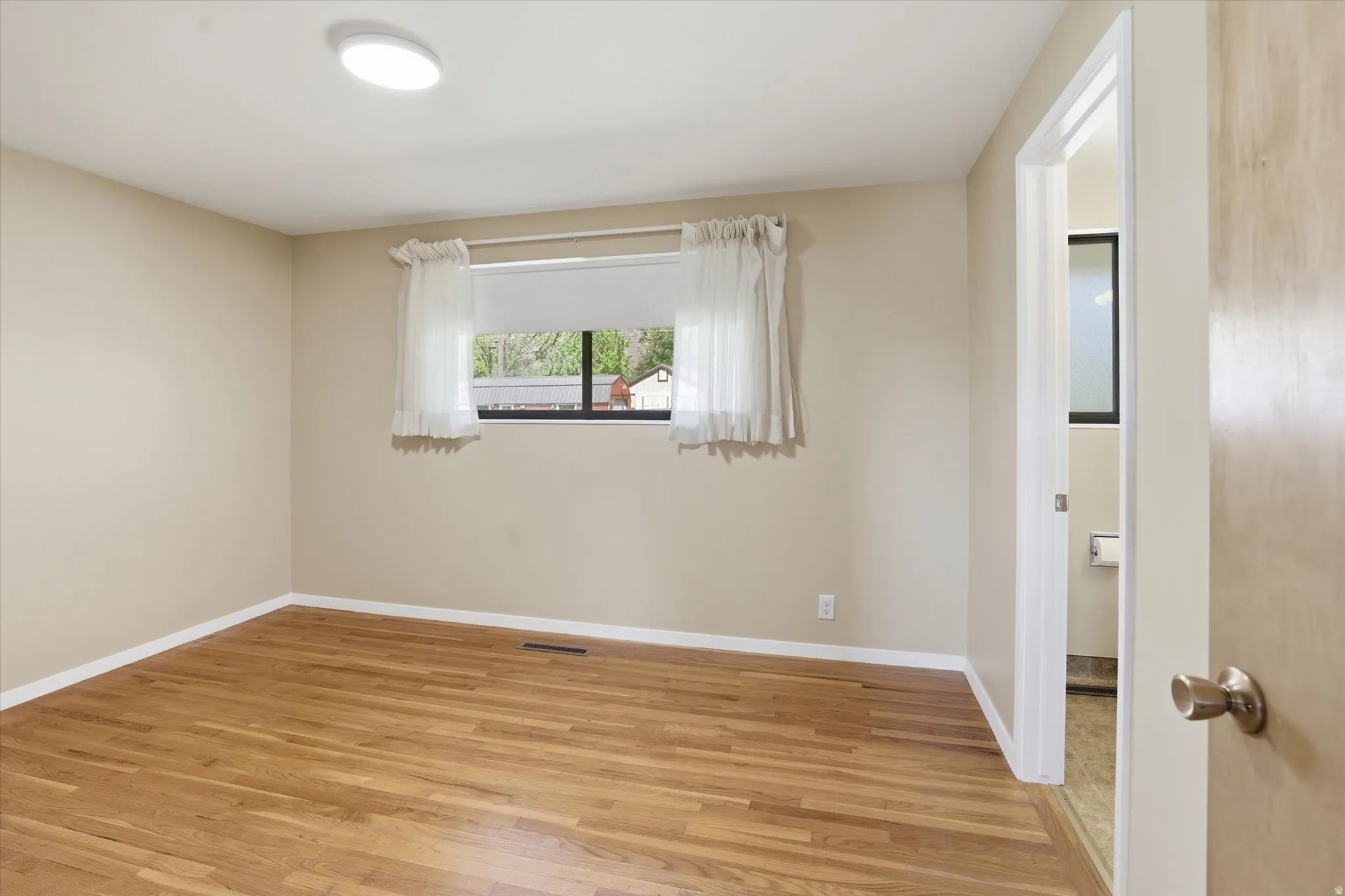 Room featuring wood-finish flooring, neutral wall tones, a flush-mount ceiling light, and a window with white trim