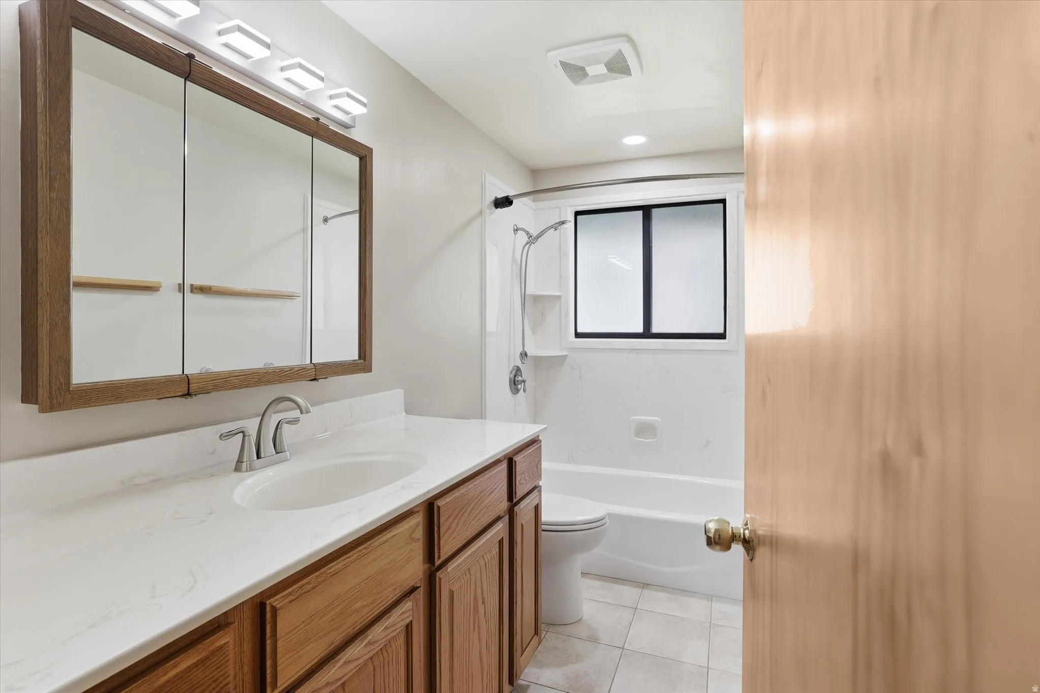 Bathroom featuring a white countertop with integrated sink, wood-finish vanity cabinetry, and a framed medicine cabinet with overhead lighting