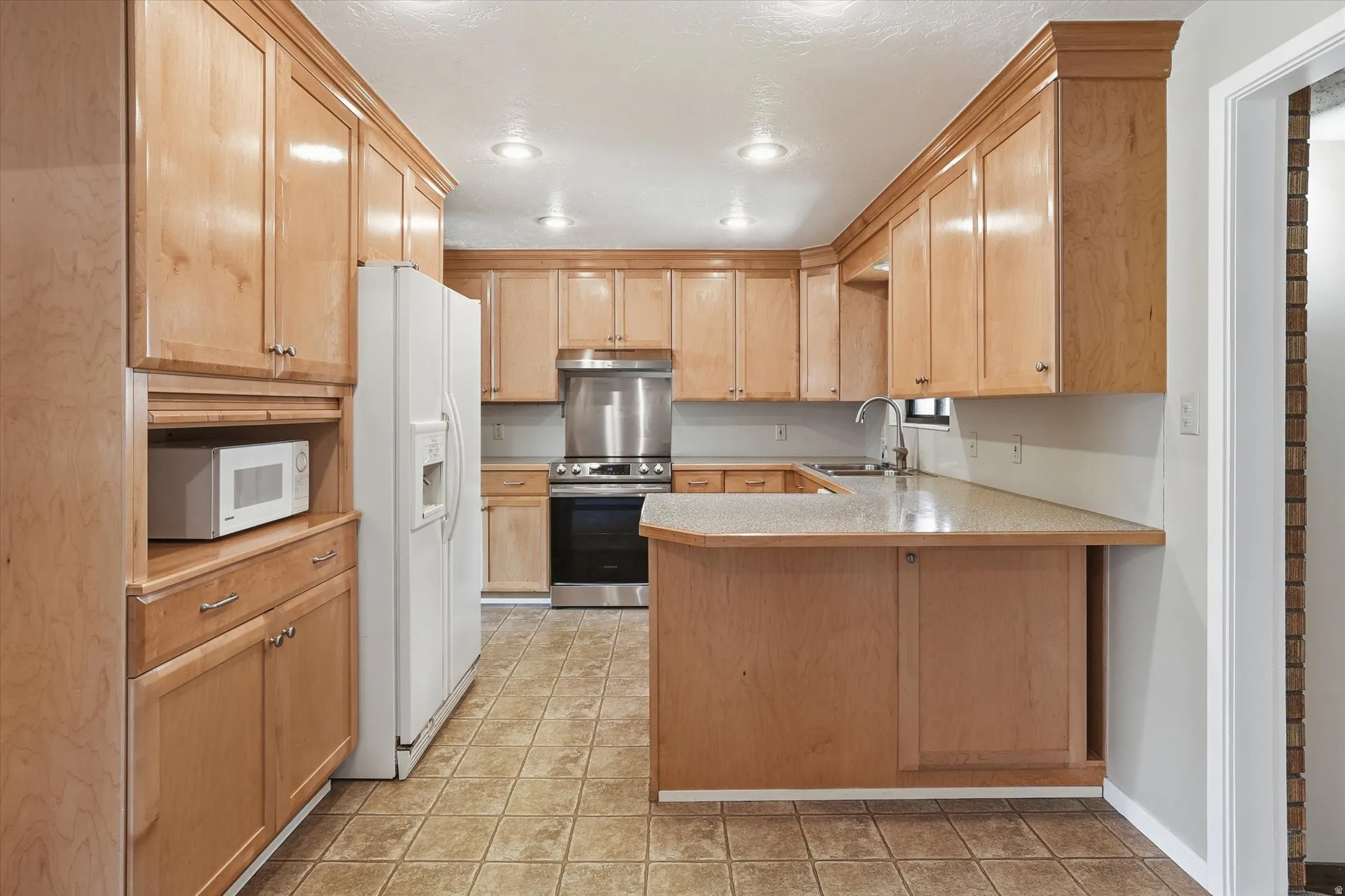 Kitchen featuring extensive light wood cabinetry with crown molding, recessed lighting, tile flooring, and a built-in microwave nook