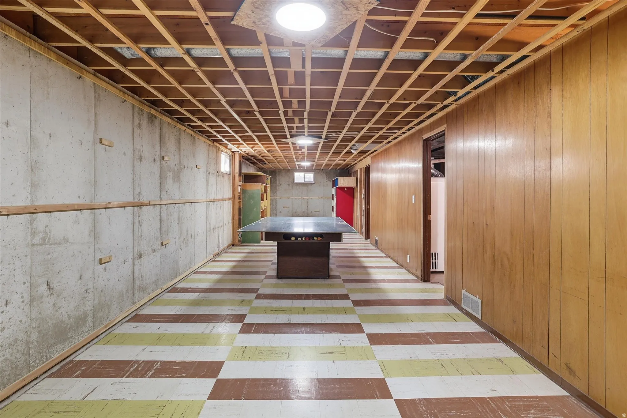 Lower level featuring concrete walls, wood paneling, exposed ceiling joists, and checkered floor tiling