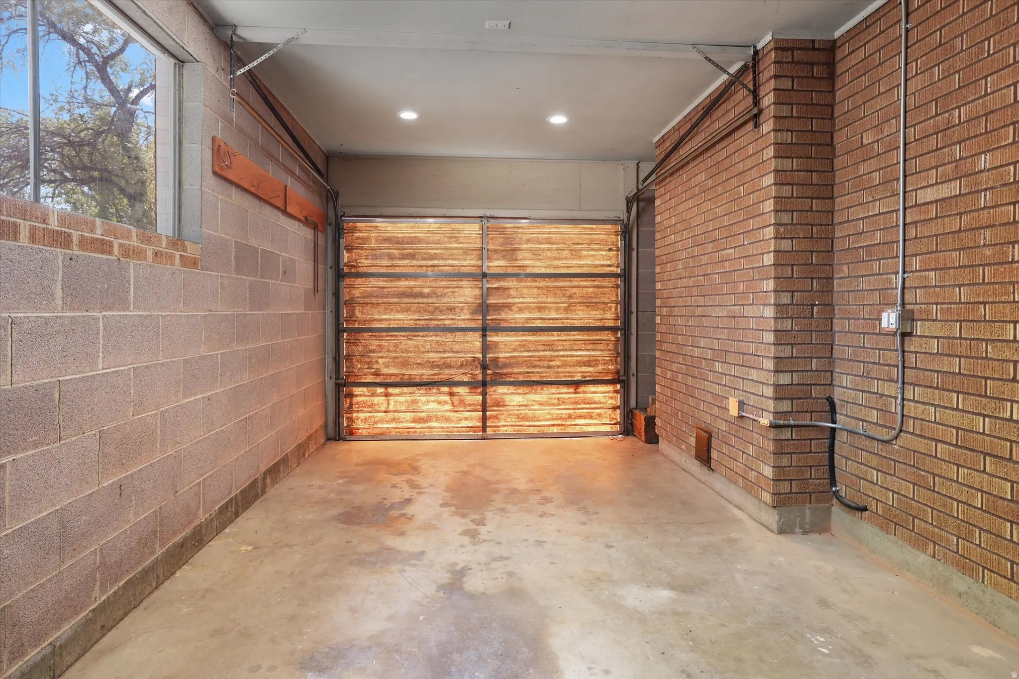 Garage space featuring a concrete floor, brick wall construction, block wall construction, a window, and recessed ceiling lighting