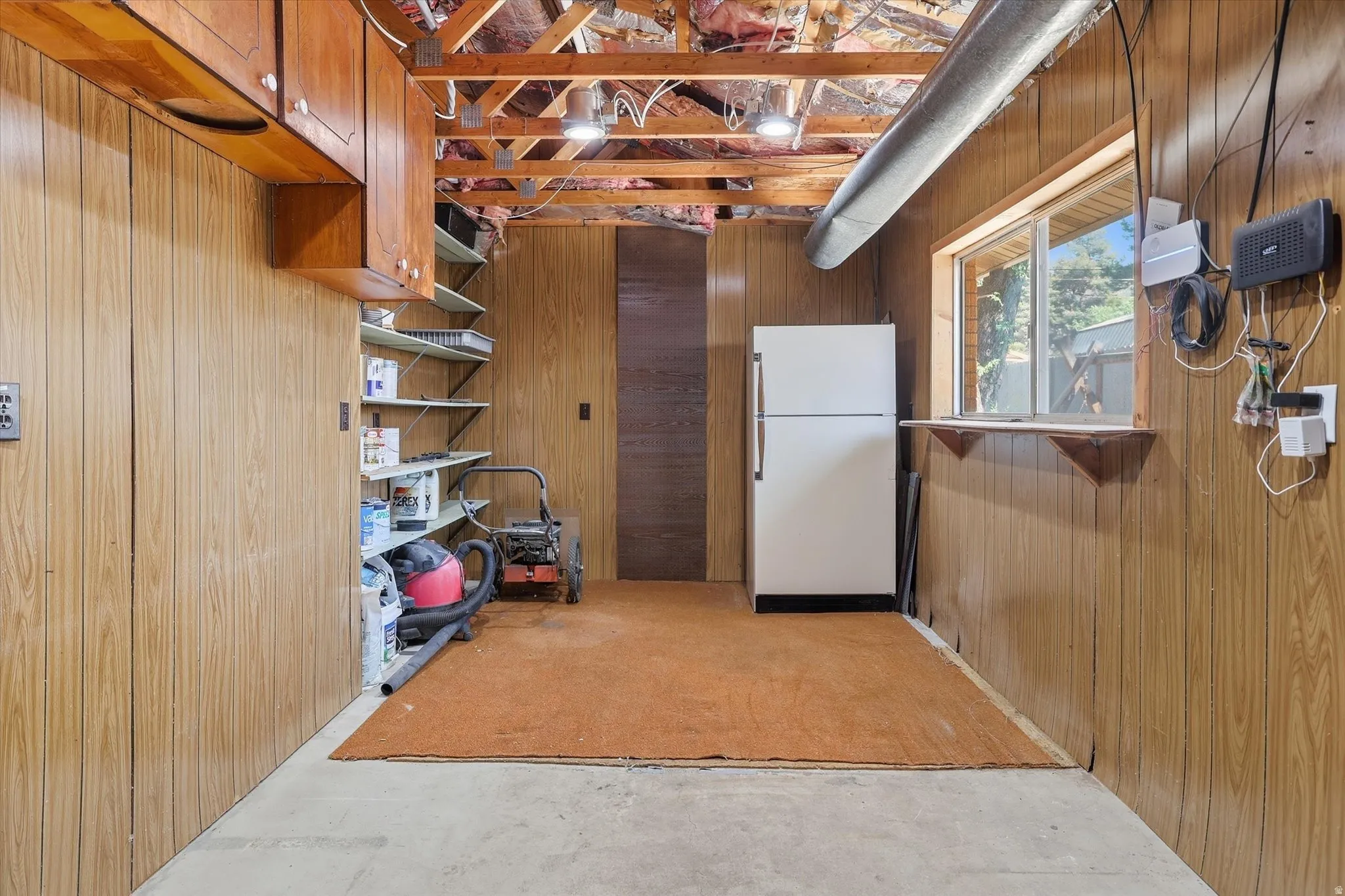 Utility space featuring wood-paneled walls, exposed ceiling joists, overhead lighting, a built-in window shelf, and a concrete floor