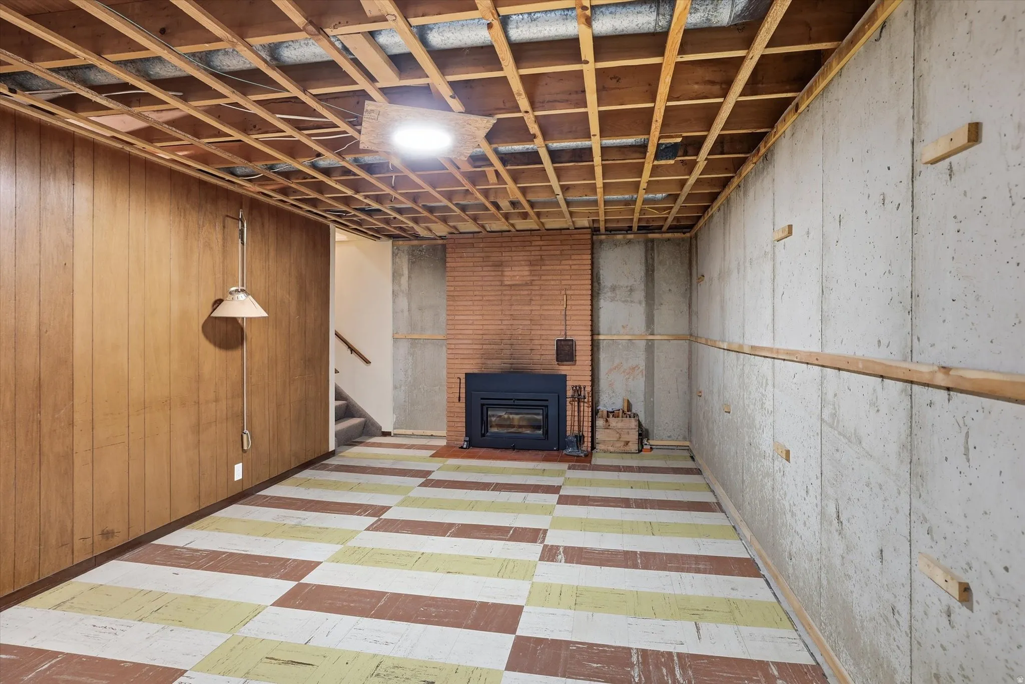 Lower level space featuring wood paneling, exposed ceiling joists, and a brick fireplace with an insert