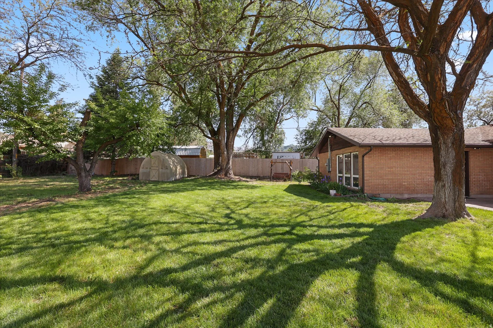 Expansive lawn area featuring mature trees, a partially visible brick exterior, and a garden structure