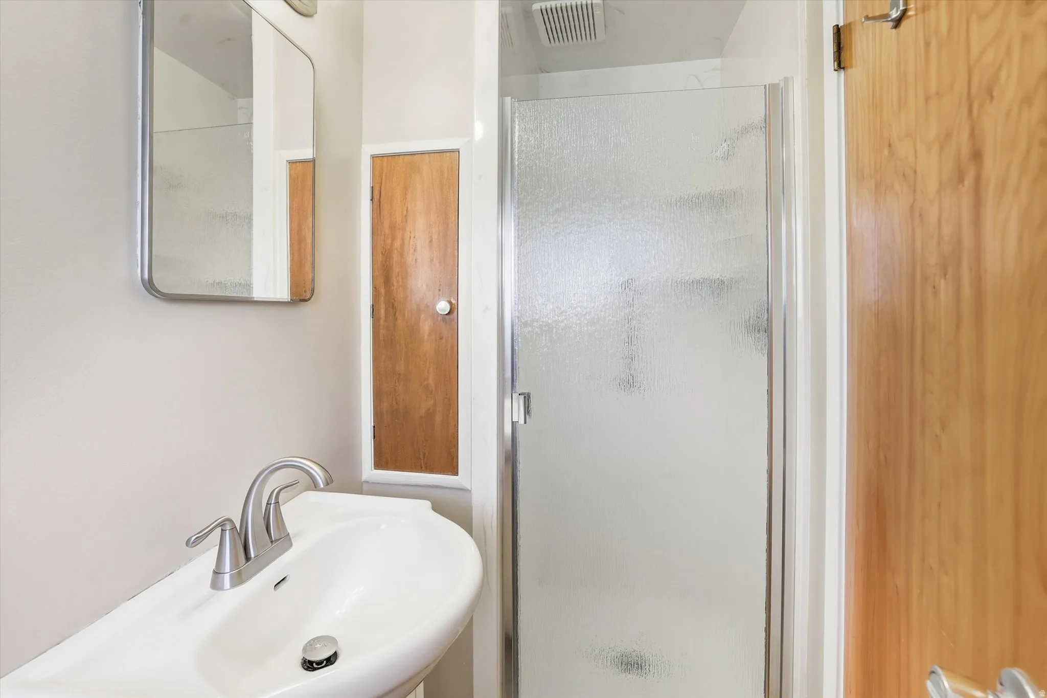 Bathroom featuring a walk-in shower with a framed glass enclosure, a wall-mounted sink with a chrome faucet, and a wall-mounted mirror