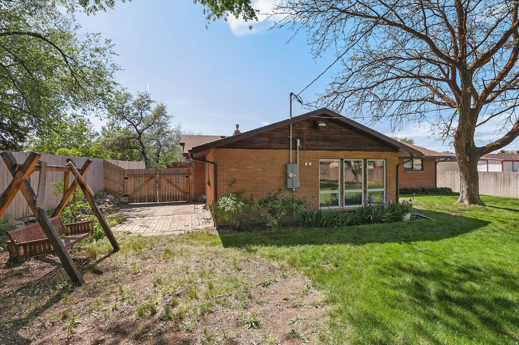 Fenced backyard featuring a brick patio, mature trees, and a wooden privacy fence with double gates