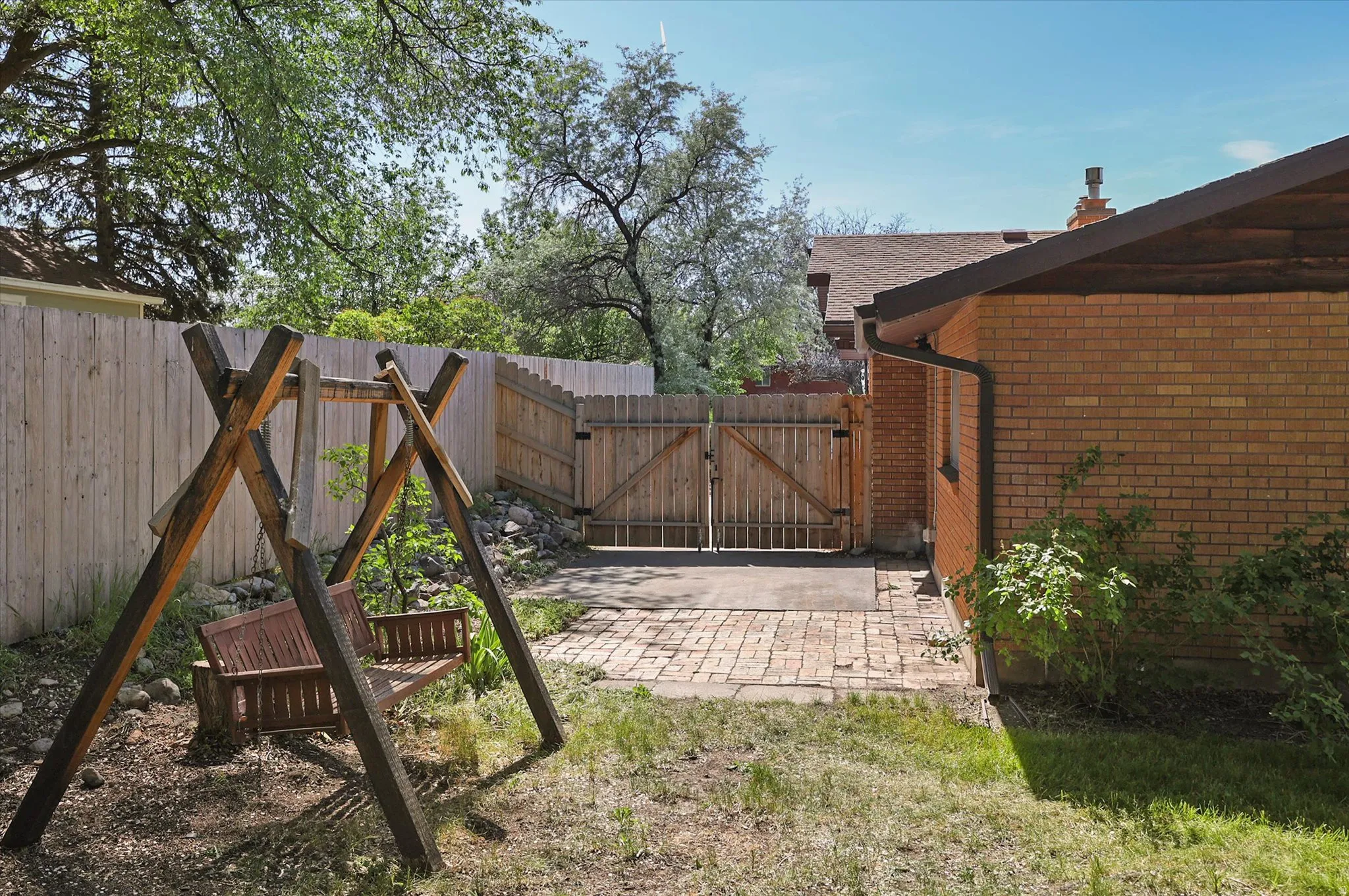 Backyard space featuring a wooden privacy fence, brick patio, and a brick exterior building with a brown roofline