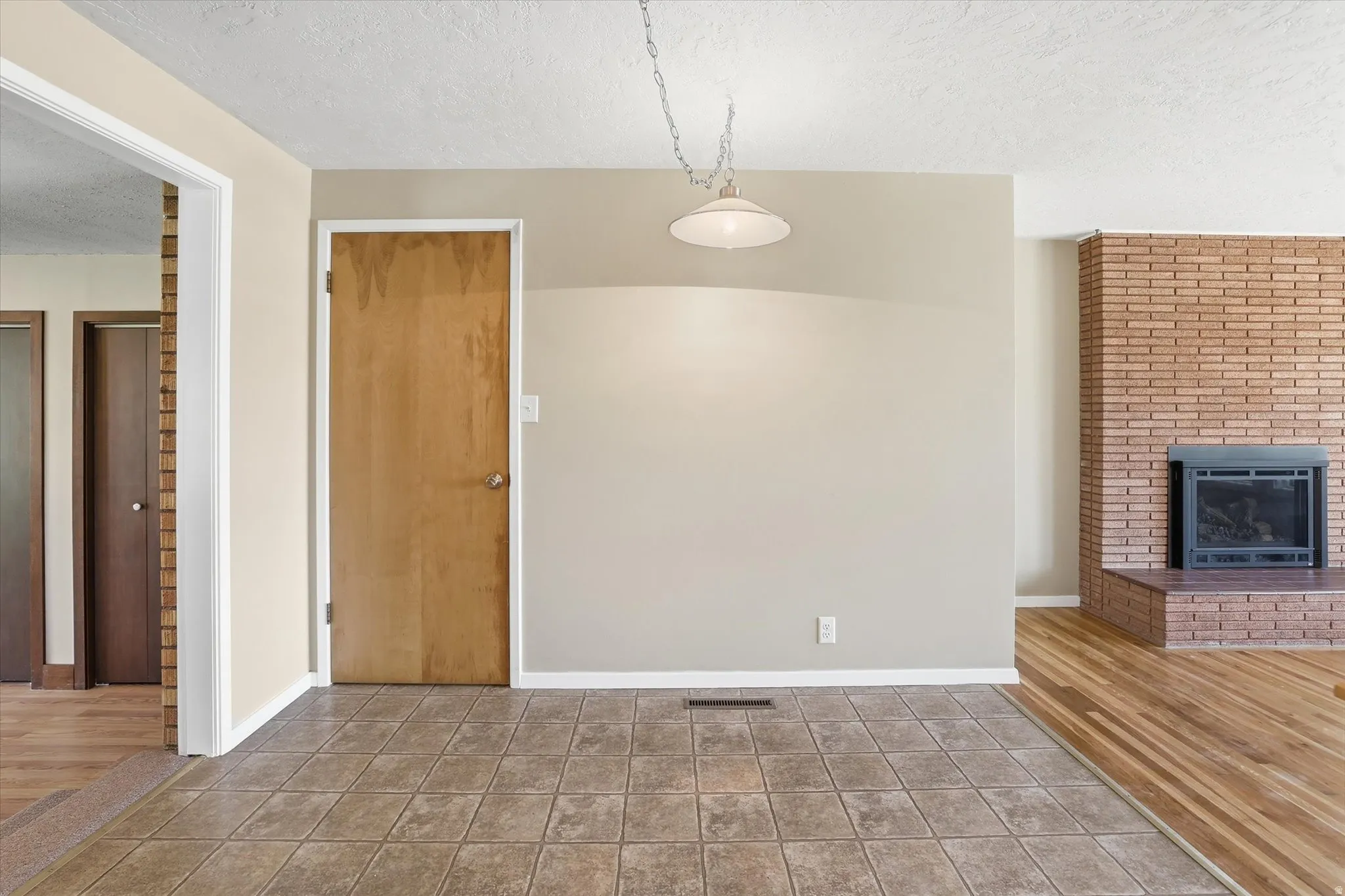 Interior space featuring a brick fireplace with a black insert, wood-finish flooring, and a tiled entry area