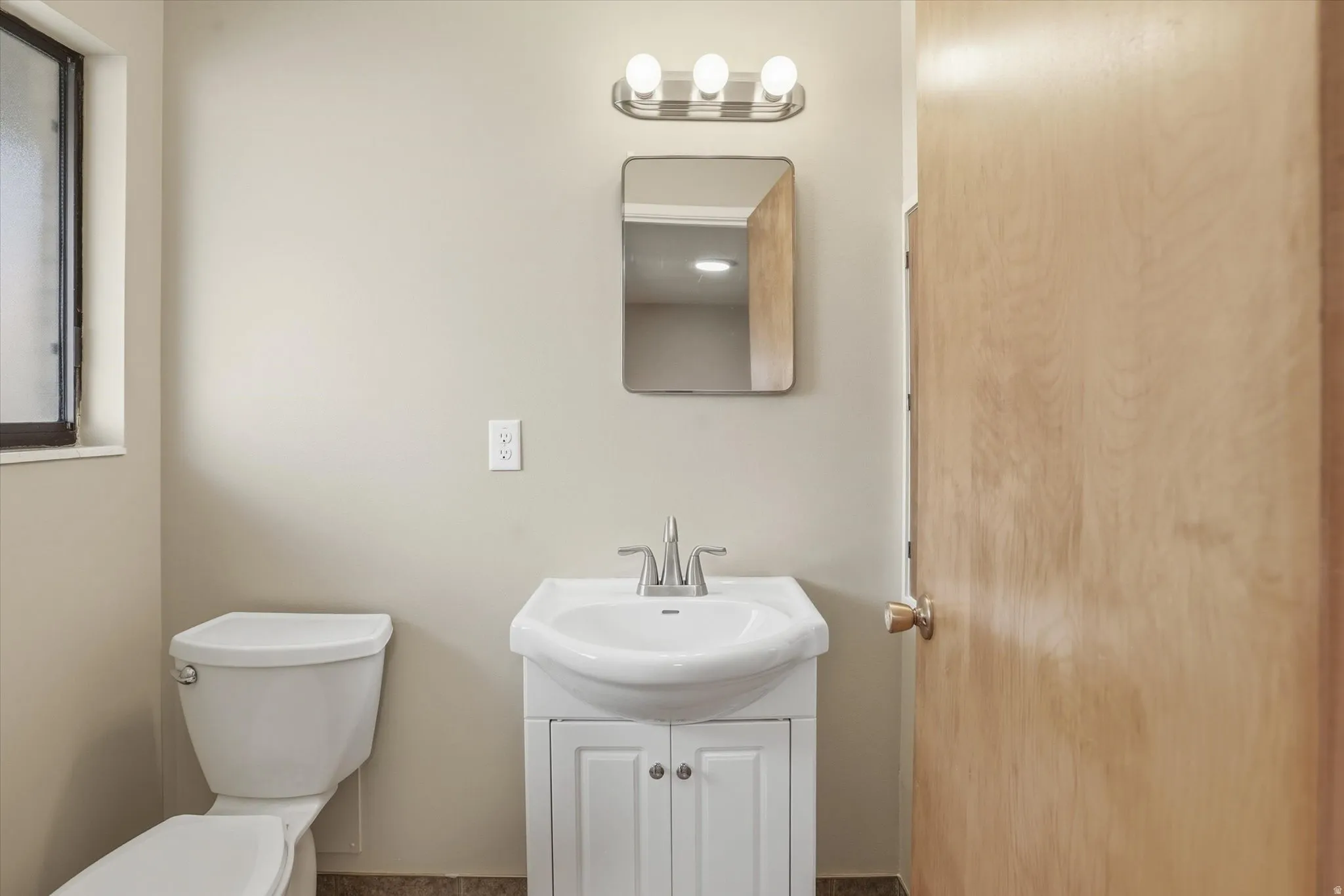 Bathroom featuring a vanity with an integrated sink, a rectangular mirror, and a three-light fixture