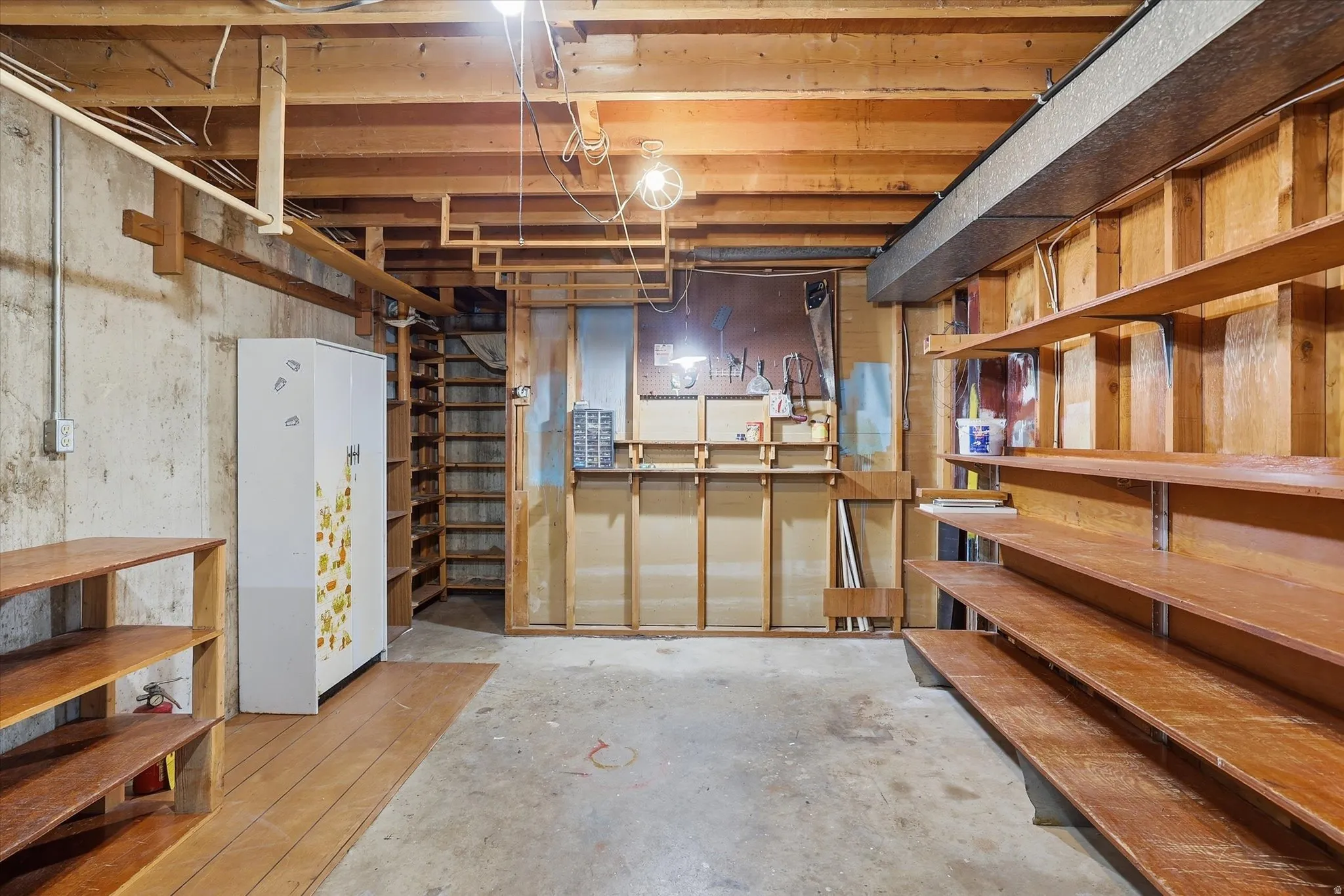 Unfinished basement featuring extensive built-in shelving, exposed wood joists, concrete flooring, and a utility area with a workbench