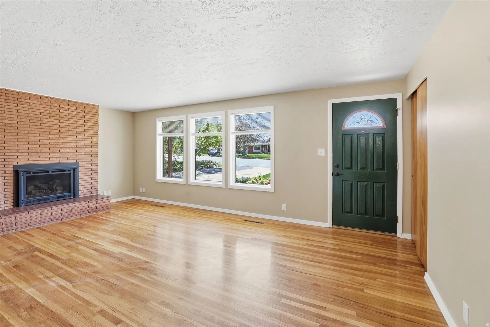 Spacious room featuring wood-finish flooring, a brick fireplace with hearth, and multiple windows
