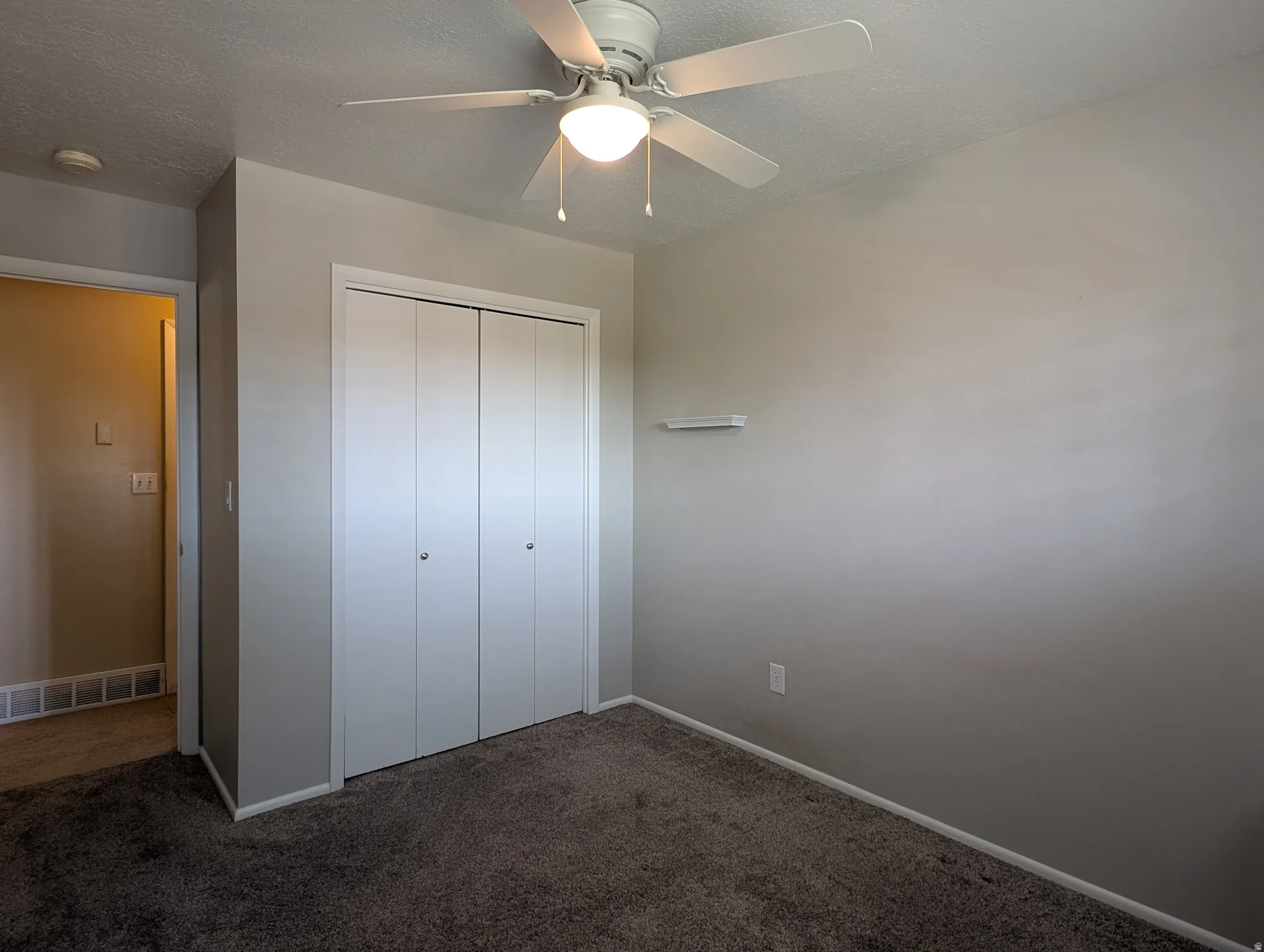 Bedroom featuring neutral gray walls, dark gray carpeting, and a white ceiling fan with integrated lighting