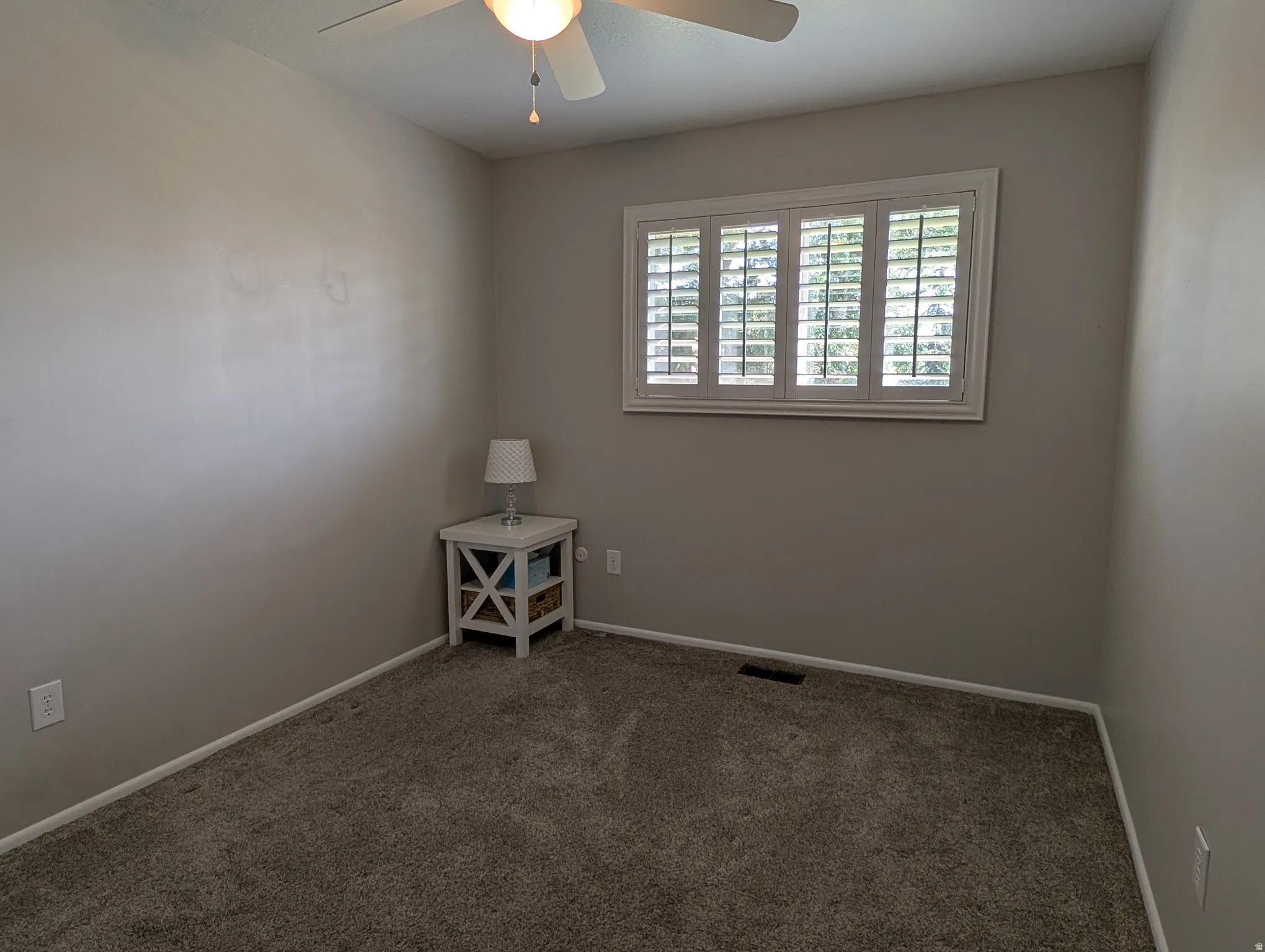 Bedoom featuring textured carpet flooring, neutral painted walls, and a window with white plantation shutters