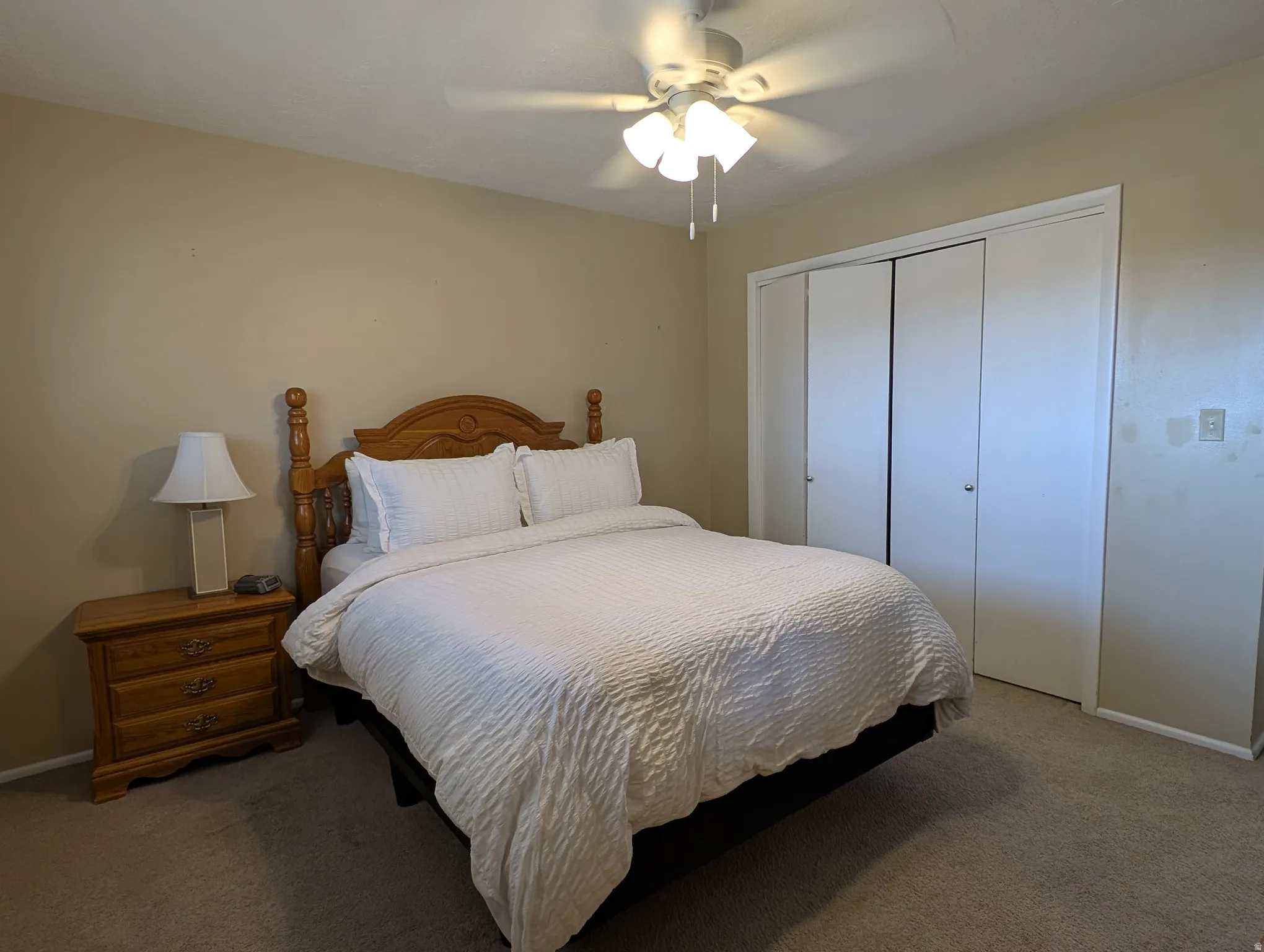 Carpeted bedroom featuring a ceiling fan with light fixture and bi-fold closet doors