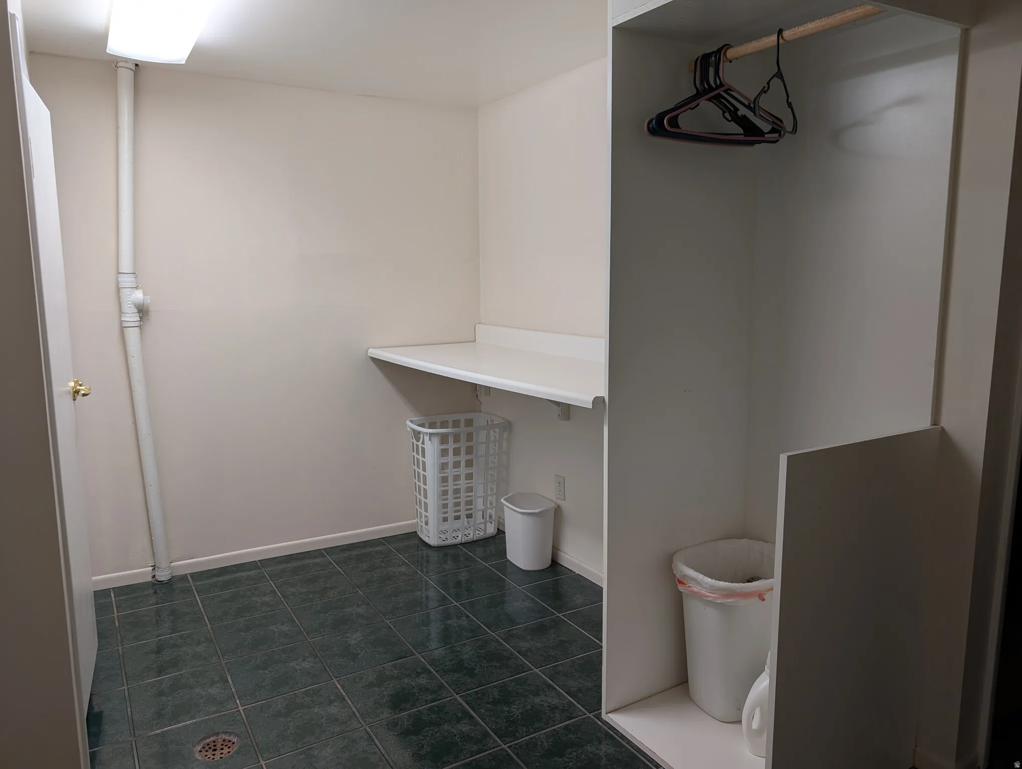Laundry area featuring dark green square floor tiles, a built-in white countertop, and a clothes hanging rod within an alcove