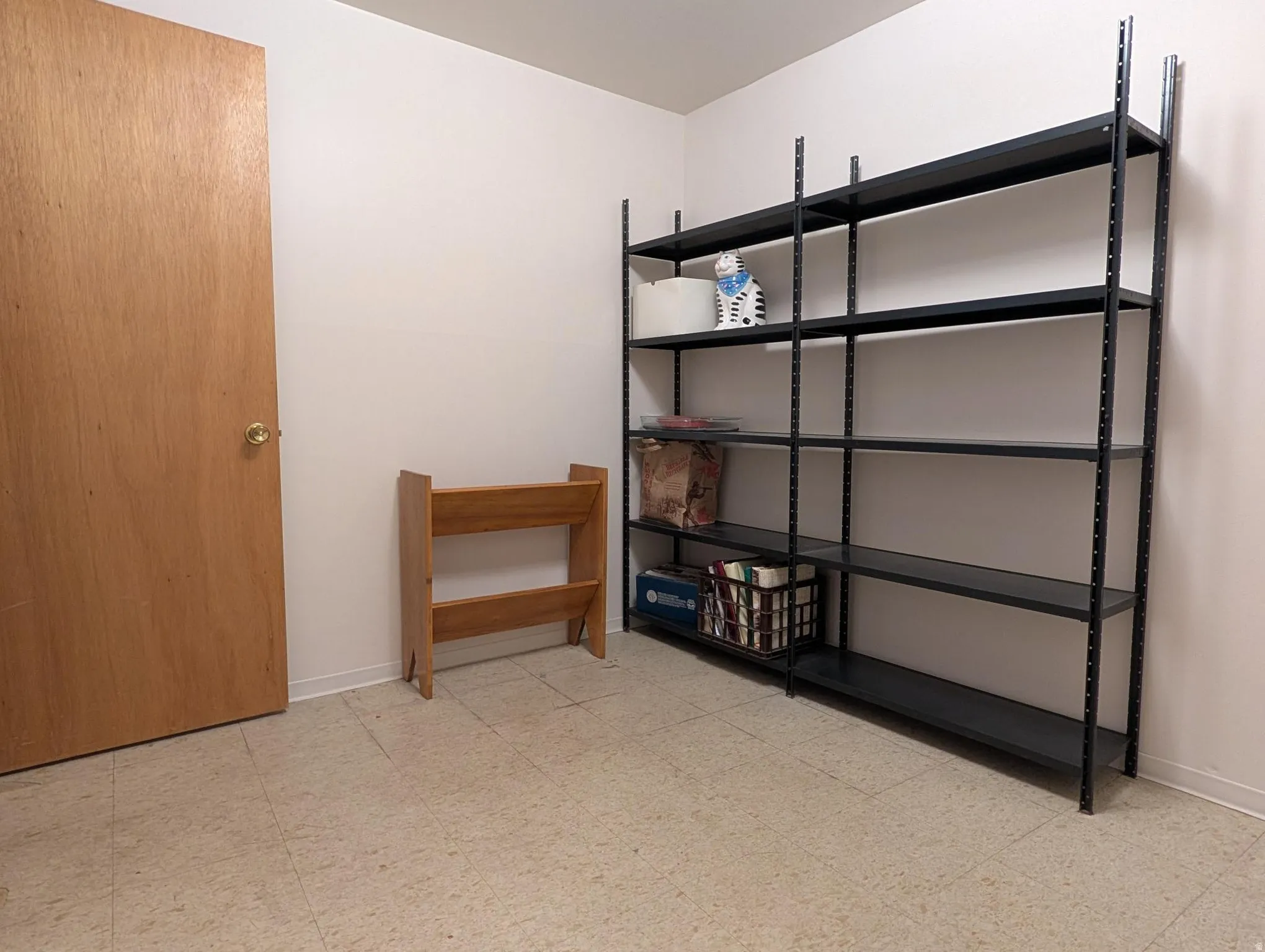 Utility/craft room featuring light-toned flooring, a light wood-finish door, and a built-in shelving unit providing extensive storage