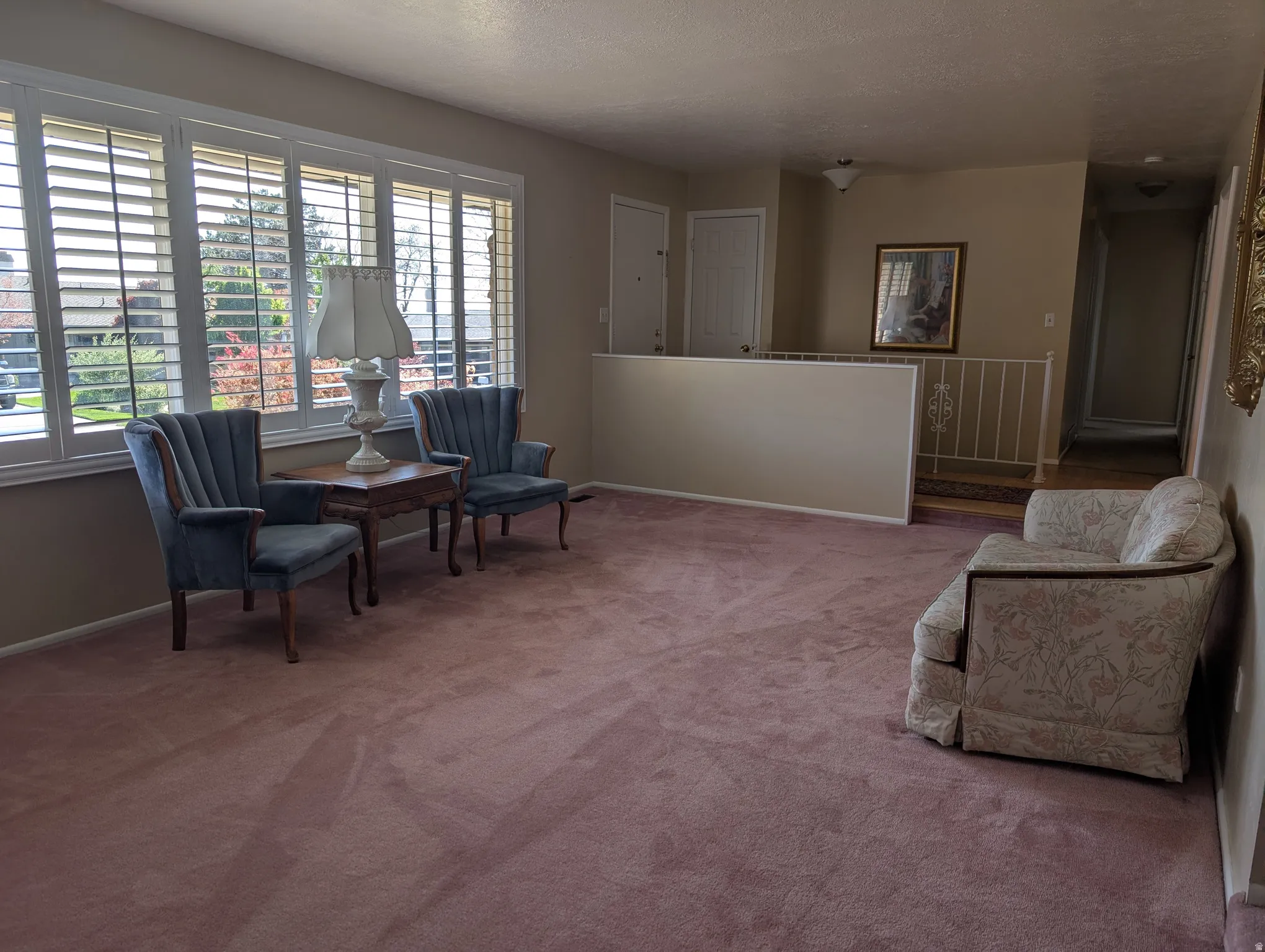 Spacious living room featuring a wall of shuttered windows, plush carpeting, and a built-in half-wall with a decorative metal railing