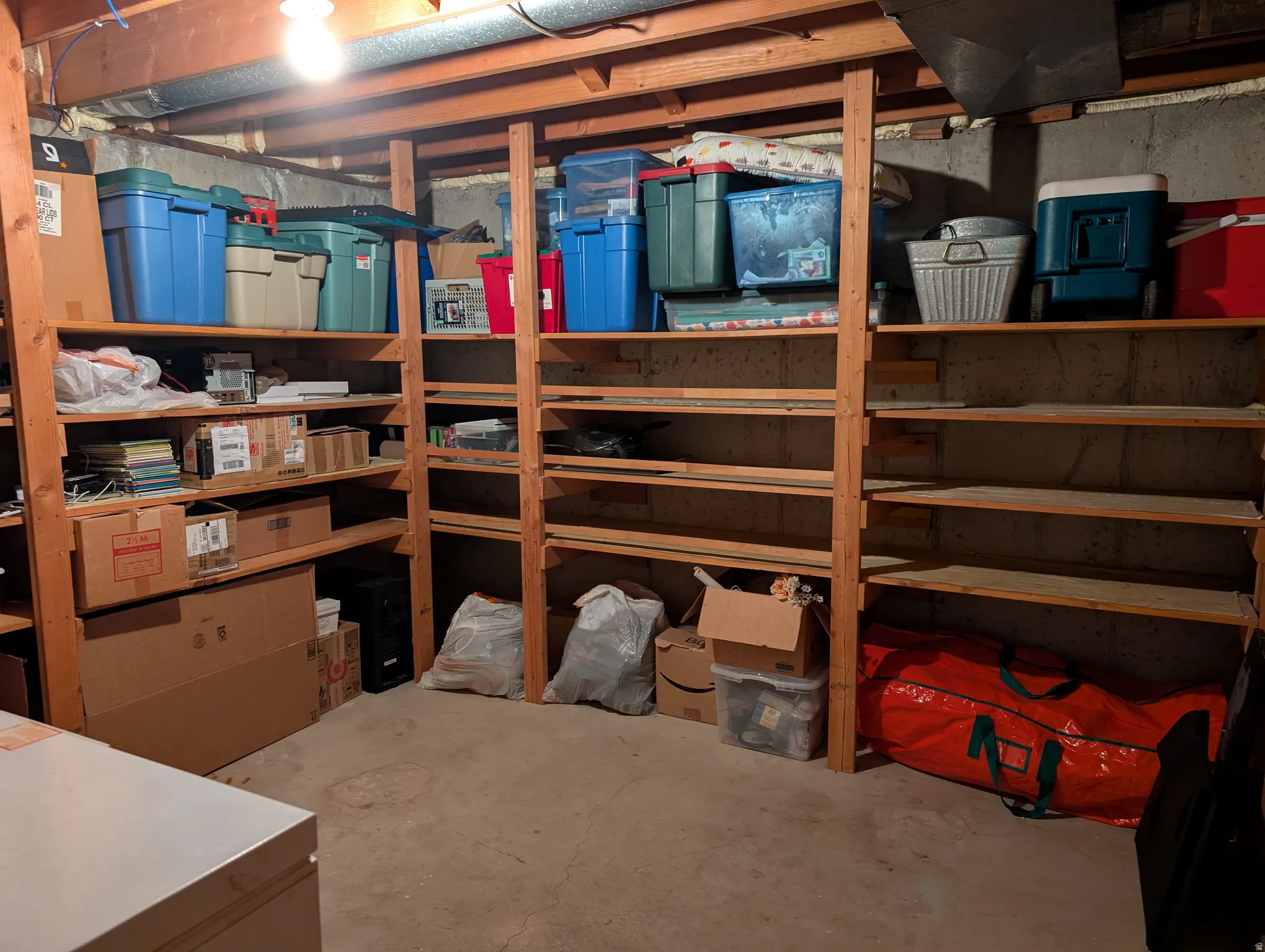 Unfinished basement area featuring extensive built-in wooden shelving for ample storage, concrete block walls, exposed wood ceiling joists, and a concrete floor