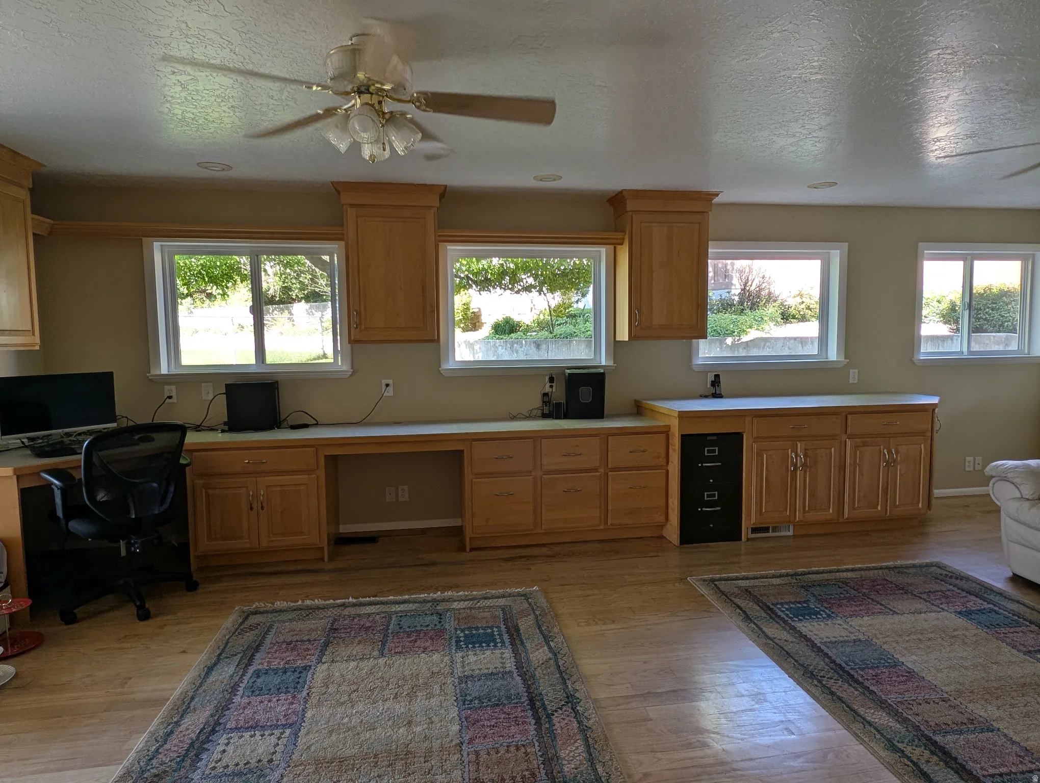 Spacious room featuring multiple windows, extensive built-in cabinetry, wood-finish flooring, a ceiling fan, and recessed lighting